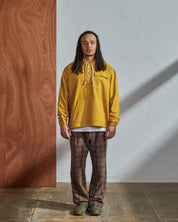 Full-length front view of model wearing Uskees yellow coloured buttoned smock, paired with brown check trousers.