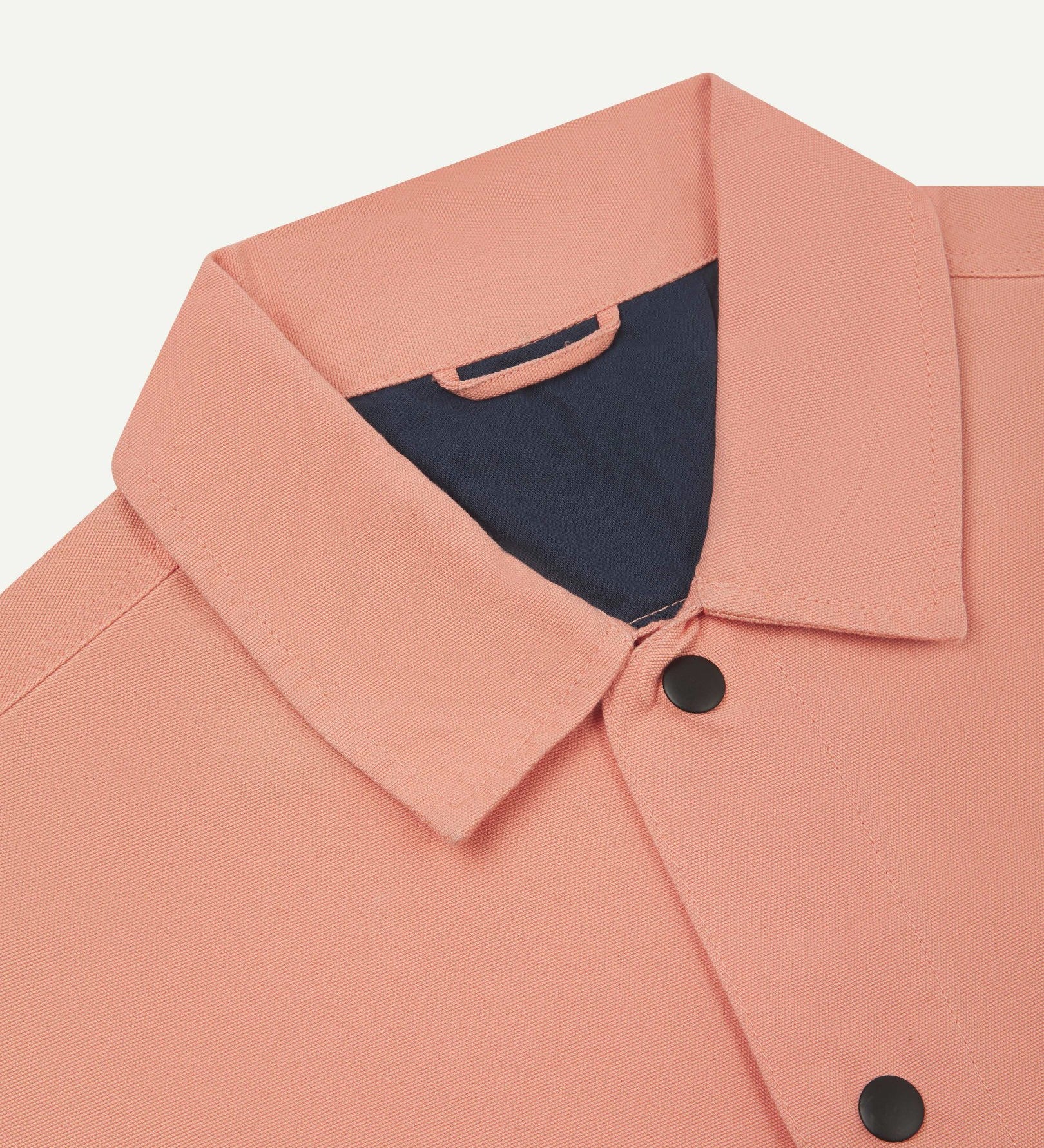 Neck view of Uskees 3013 pink-orange (coral) organic cotton coach jacket with focus on collar, contrast inner yoke, Uskees brand label and popper buttons.