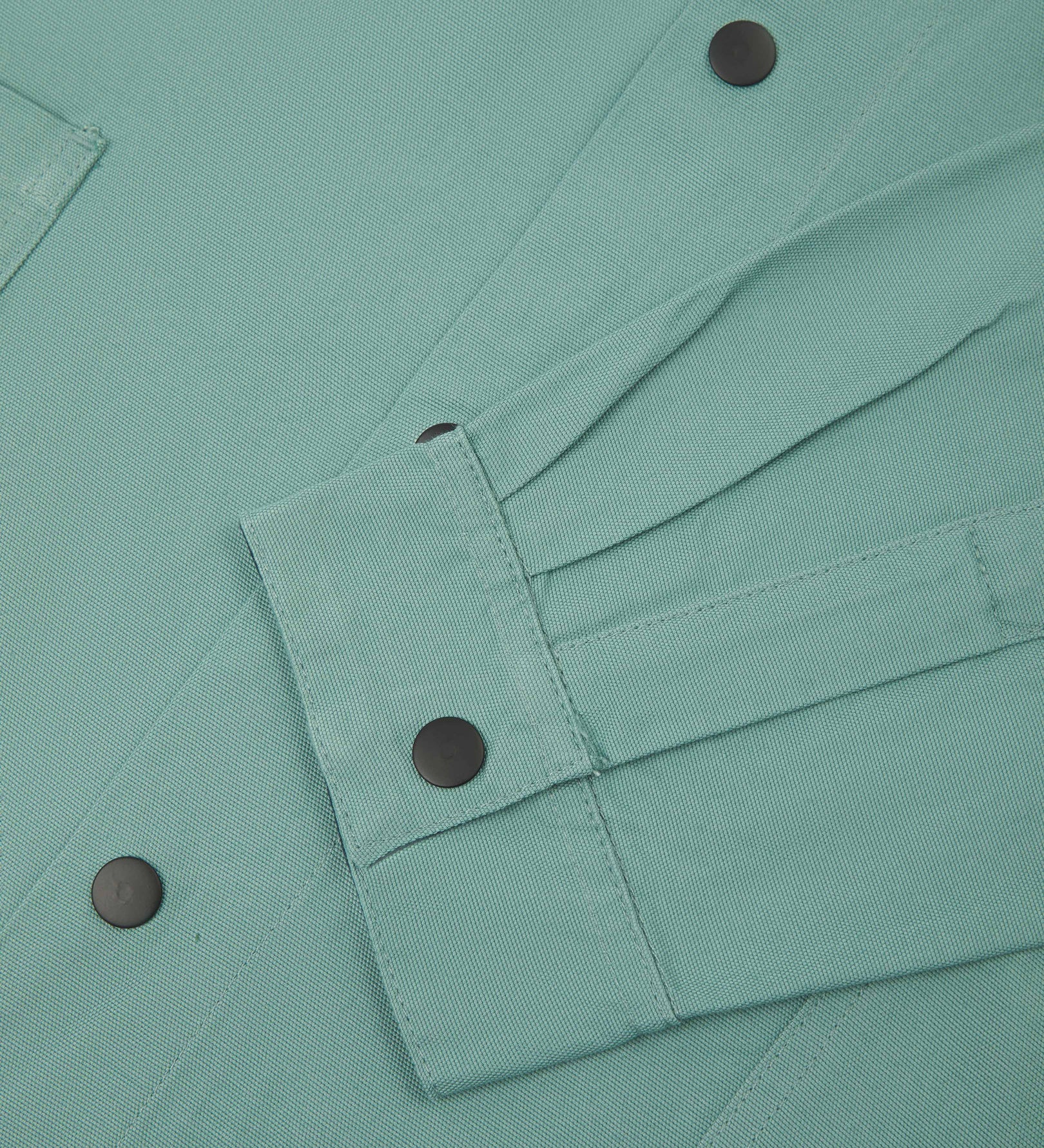 Sleeve view of Uskees 3013 eucalyptus-green organic cotton coach jacket with focus on placket, cuff and popper buttons.