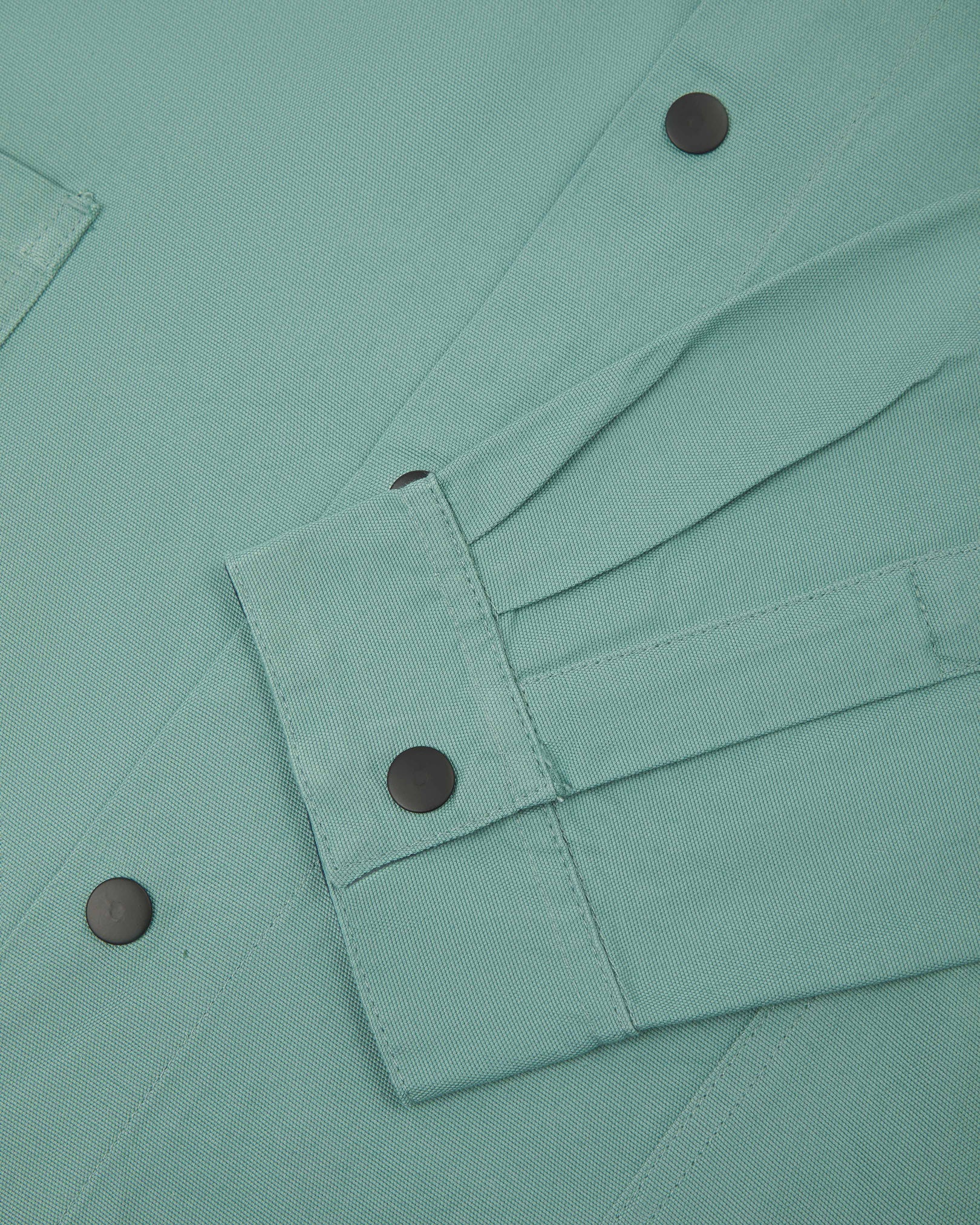 Sleeve view of Uskees 3013 eucalyptus-green organic cotton coach jacket with focus on placket, cuff and popper buttons.