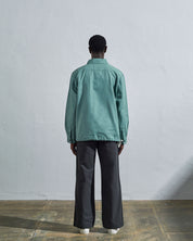 Full-length back view of model wearing Uskees Coach's jacket in eucalyptus blue-green, illustrating reinforced elbow and simple, boxy silhouette. 