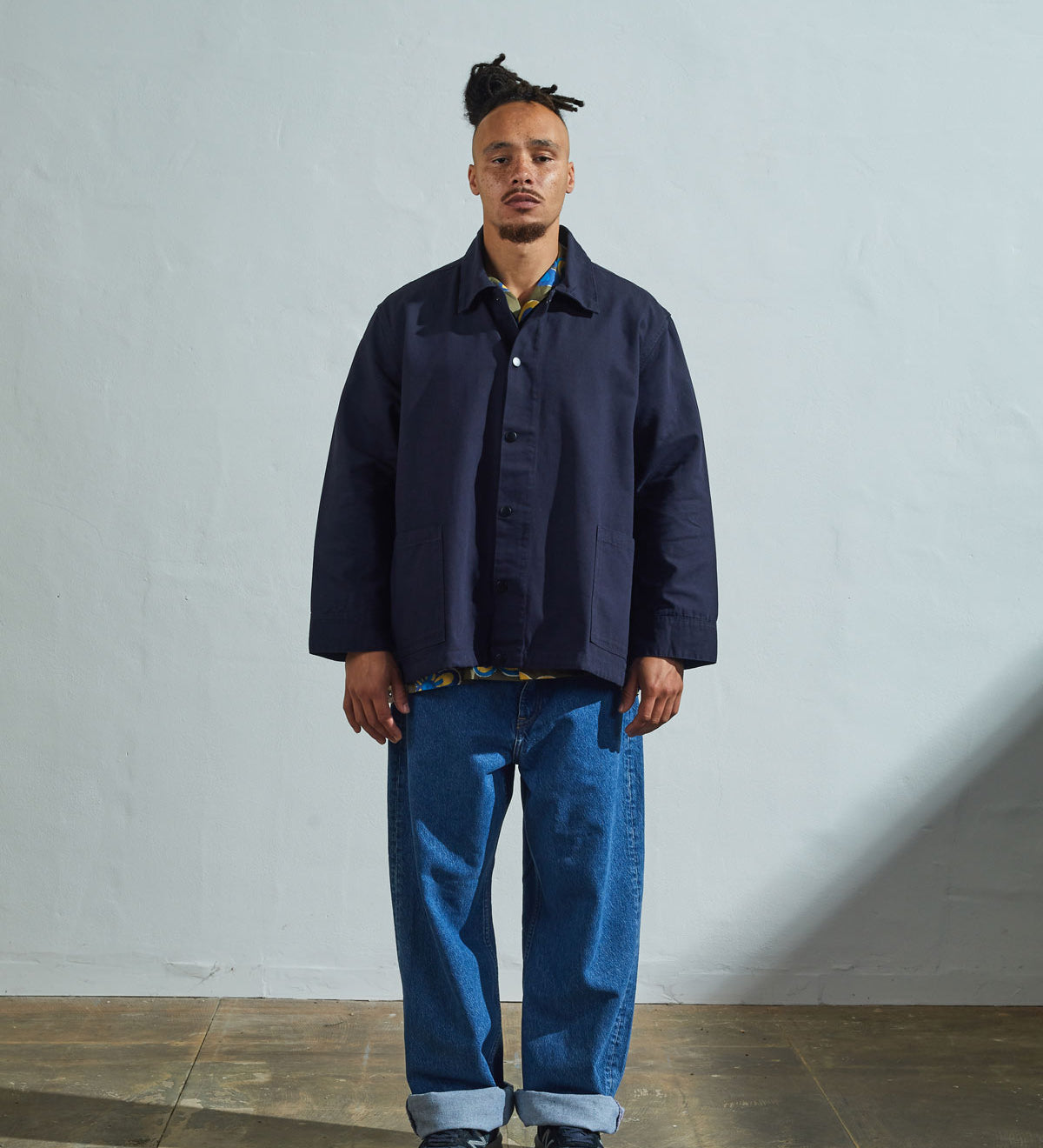 Model front view wearing Uskees coach's jacket in a discontinued size in midnight blue paired with loose-fitting blue jeans.