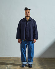 Model front view wearing Uskees coach's jacket in a discontinued size in midnight blue paired with loose-fitting blue jeans.