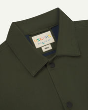 Neck view of Uskees 3013 vine green organic cotton coach jacket with focus on collar, contrast inner yoke, Uskees brand label and popper buttons.