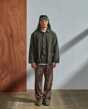 Front view of model wearing Uskees coach's jacket in a discontinued size in vine green paired with loose-fitting brown check pants.