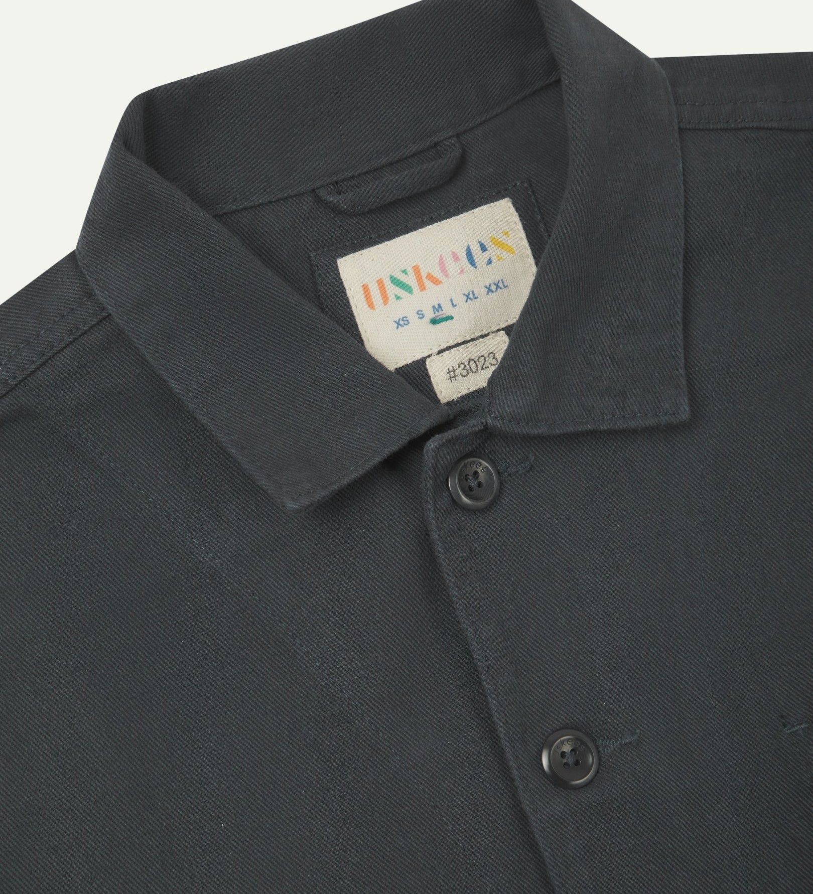 Front close view of charcoal-grey organic cotton drill commuter blazer showing dual collar and Uskees branding label.