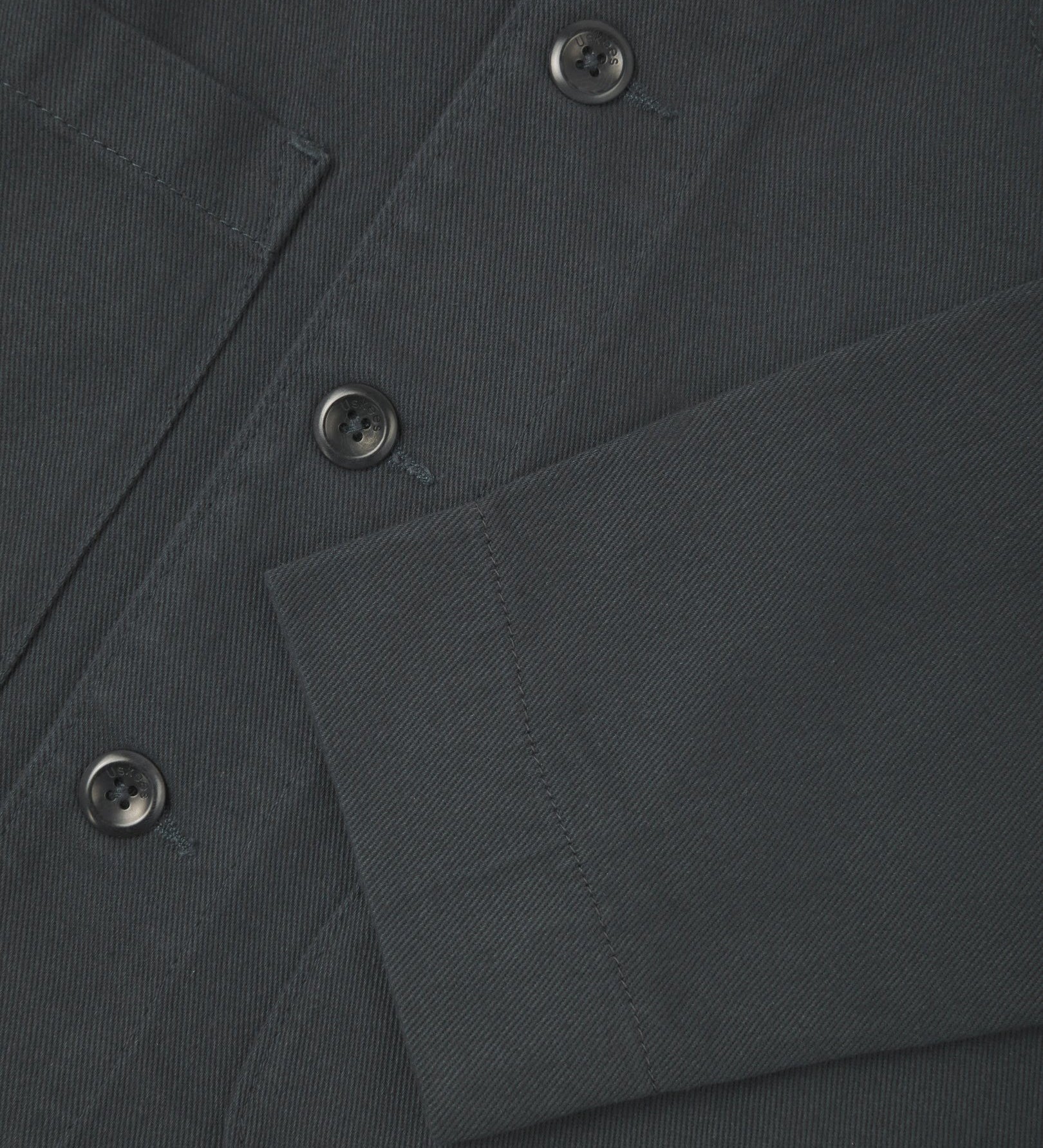 Close up view of charcoal-grey organic cotton drill commuter blazer showing front buttons and cuff detail.