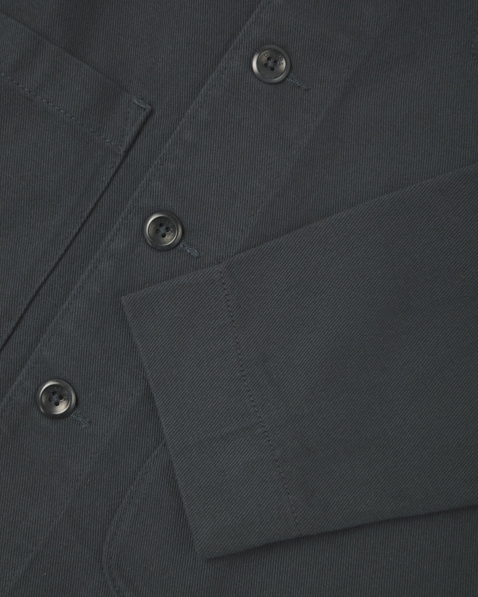 Close up view of charcoal-grey organic cotton drill commuter blazer showing front buttons and cuff detail.