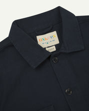 Close-up top-half view of #3024, dark blue (blueberry)-coloured organic cotton-drill over shirt. With focus on collar, Uskees brand label and corozo buttons.
