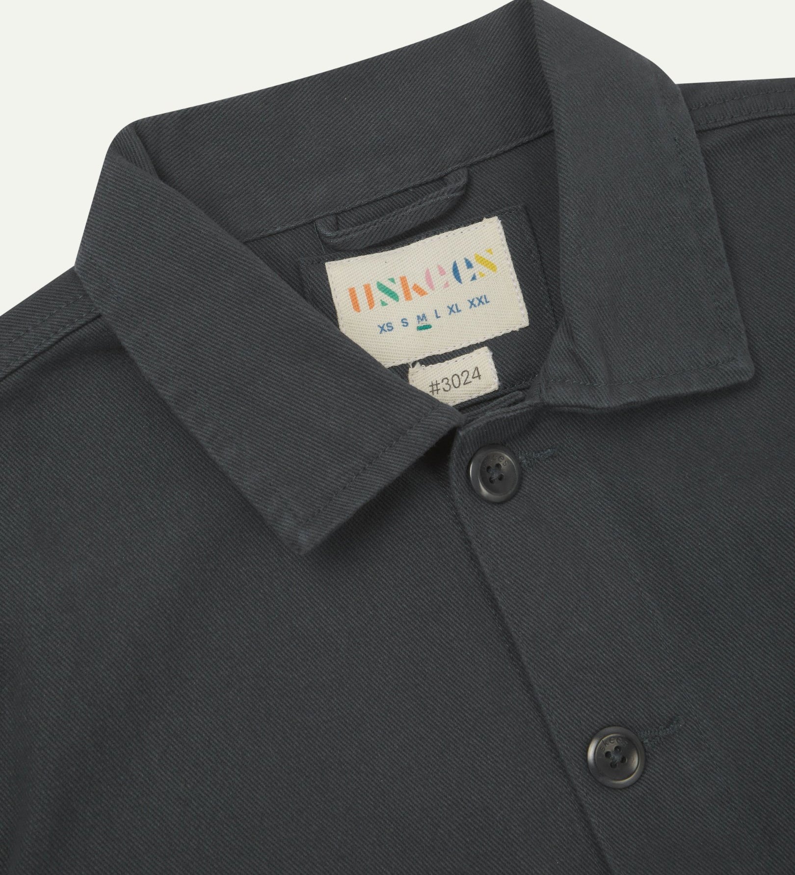 Close-up top-half view of #3024, charcoal-grey organic cotton drill over shirt. With focus on collar, Uskees brand label and corozo buttons.