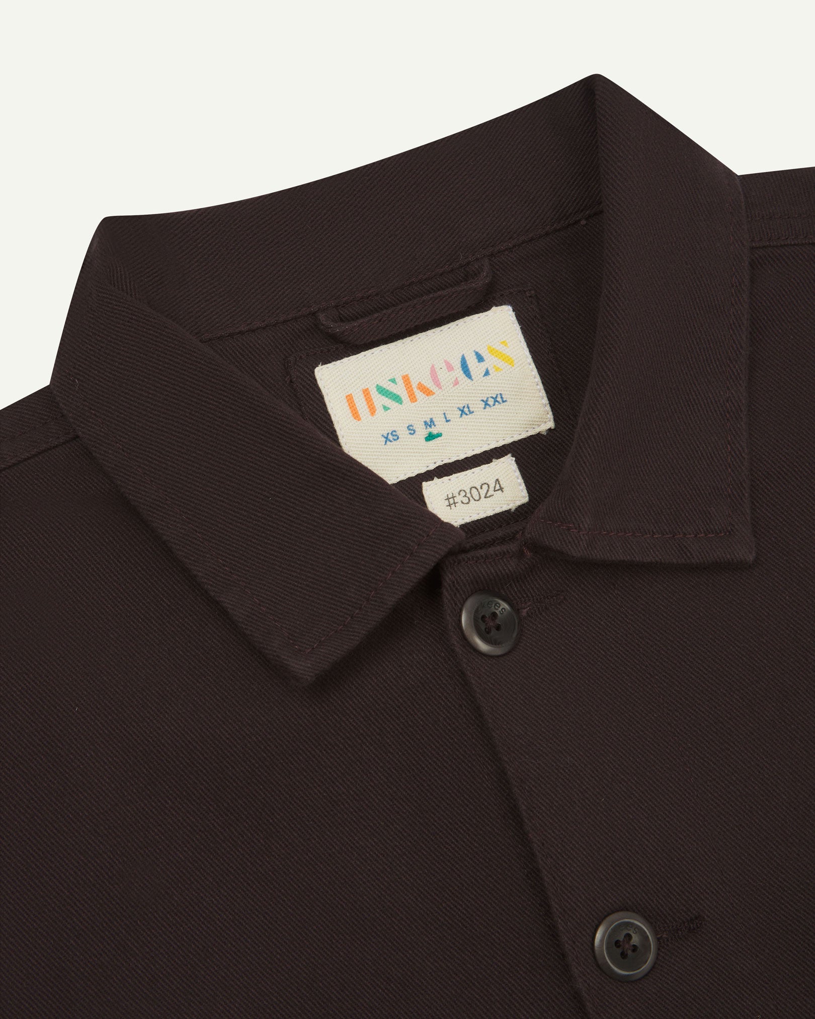 Close-up top-half view of #3024, burgundy-brown-coloured organic cotton-drill over shirt. With focus on collar, Uskees brand label and corozo buttons.