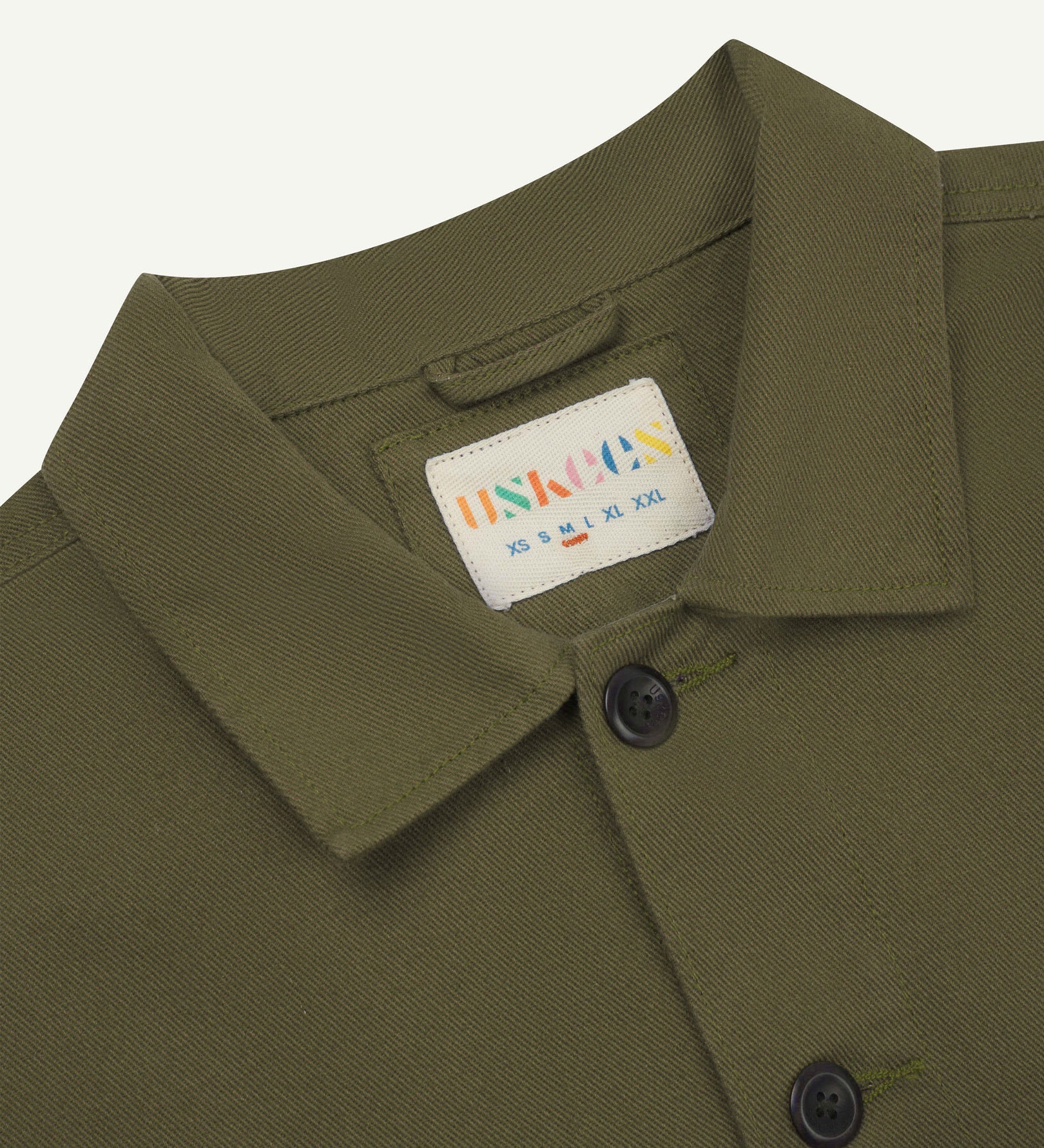 Close-up top-half view of #3024, moss-green-coloured organic cotton-drill over shirt. With focus on collar, Uskees brand label and corozo buttons.