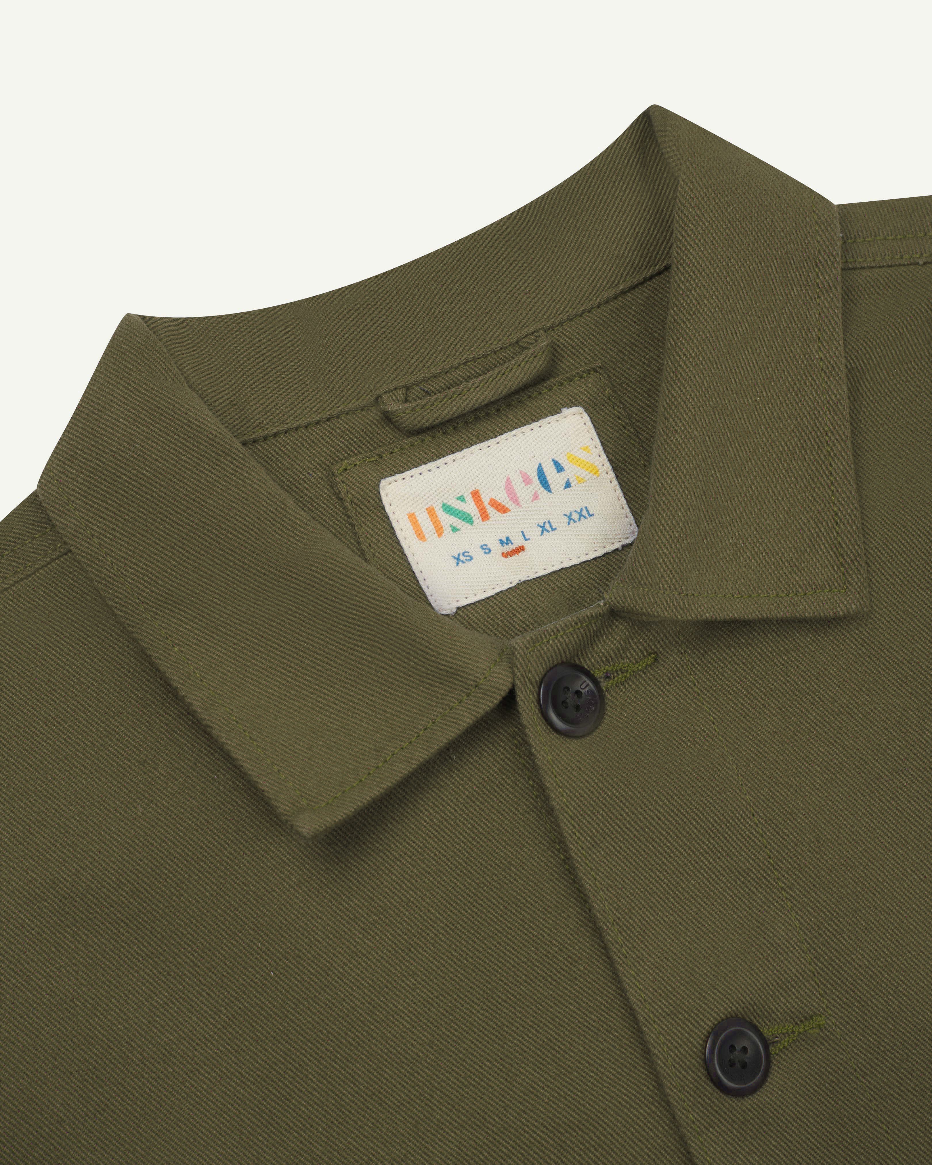 Close up shot of Uskees #3024 drill overshirt in moss showing neck label and Corozo buttons.
