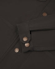 Detail shot of Uskees men's canvas chore jacket in charcoal-grey with a green collar showing the adjustable cuff, sleeve and pockets in close-up 