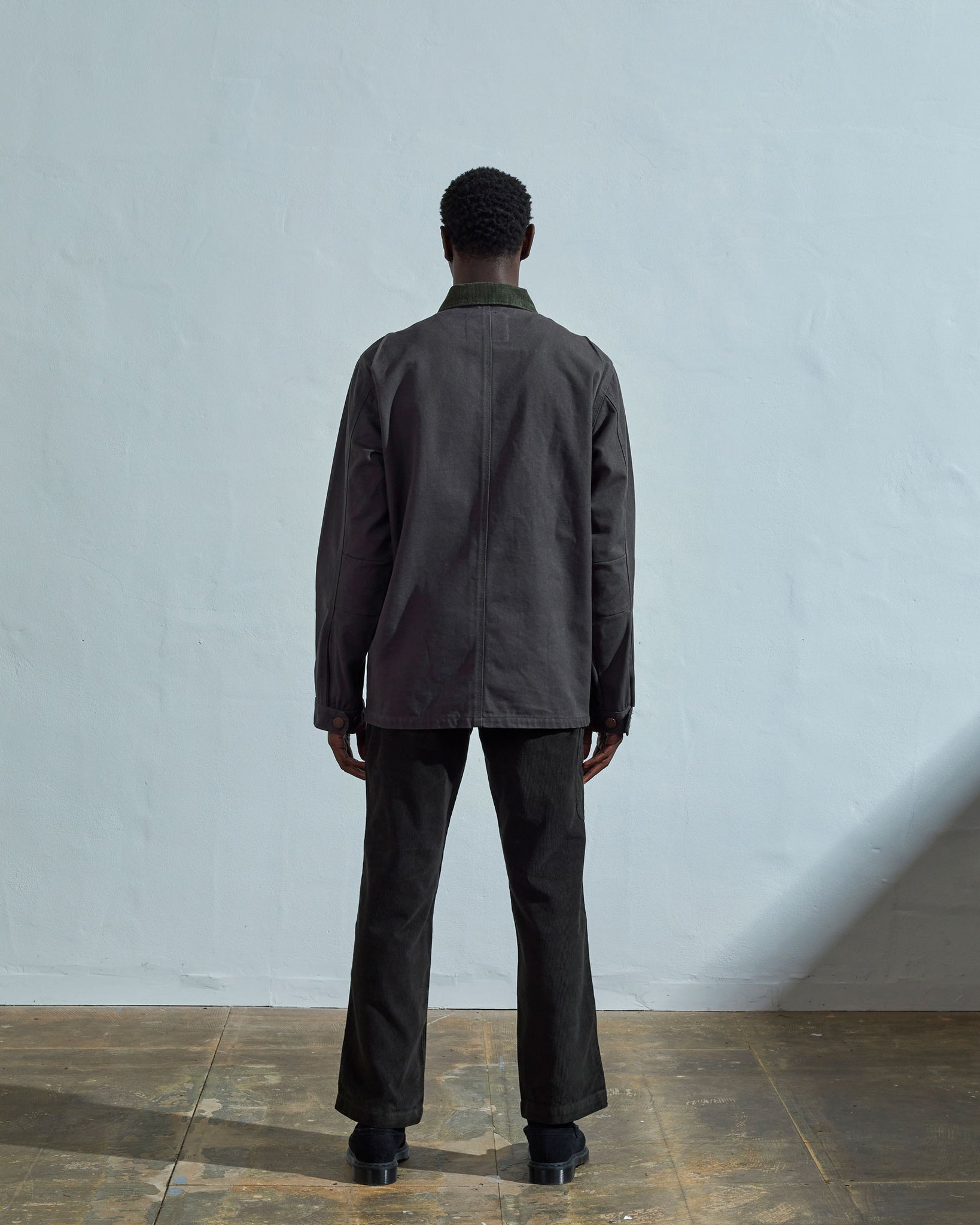 Full-length reverse view of model wearing  #3025 charcoal organic canvas chore jacket, with view of back seam and dark corduroy collar.