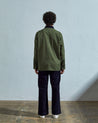 Full-length reverse view of model wearing  #3025 coriander-green organic canvas chore jacket, with view of back seam and dark corduroy collar.