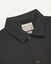 Front close-up view of Uskees dark grey canvas men's overshirt presented buttoned up showing the metal buttons, collar and brand label.