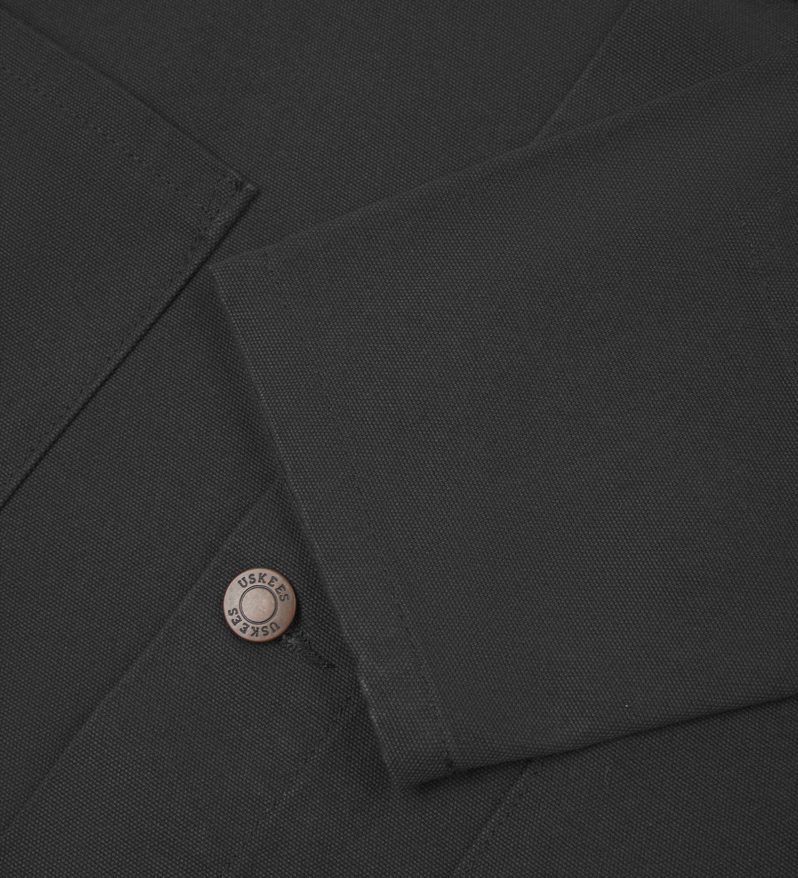 Close view of Uskees dark grey canvas men's shacket showing the cuff, sleeve and metal buttons..