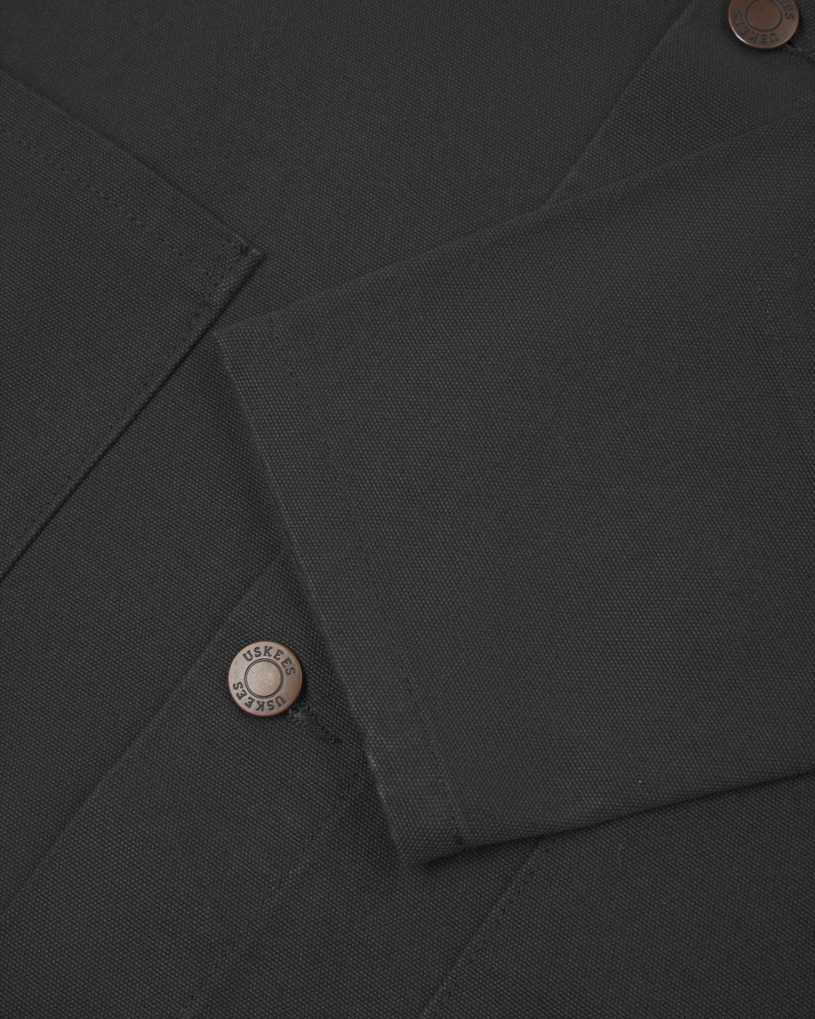 Close view of Uskees dark grey canvas men's shacket showing the cuff, sleeve and metal buttons..