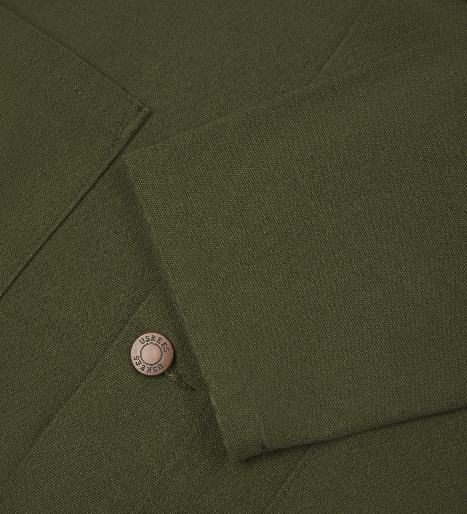 Close view of Uskees coriander-green canvas men's shacket showing the cuff, sleeve and metal buttons..