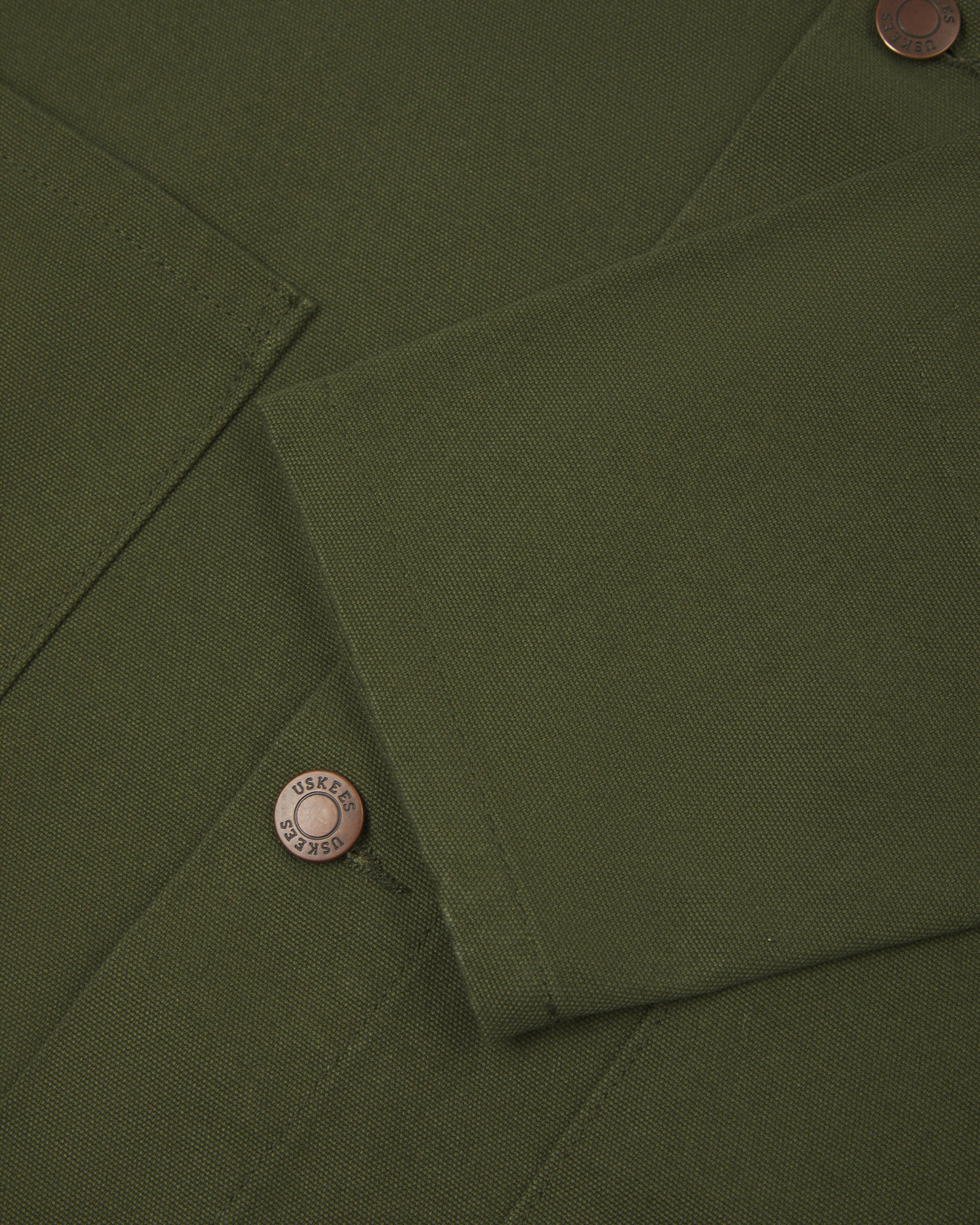 Close view of Uskees coriander-green canvas men's shacket showing the cuff, sleeve and metal buttons..