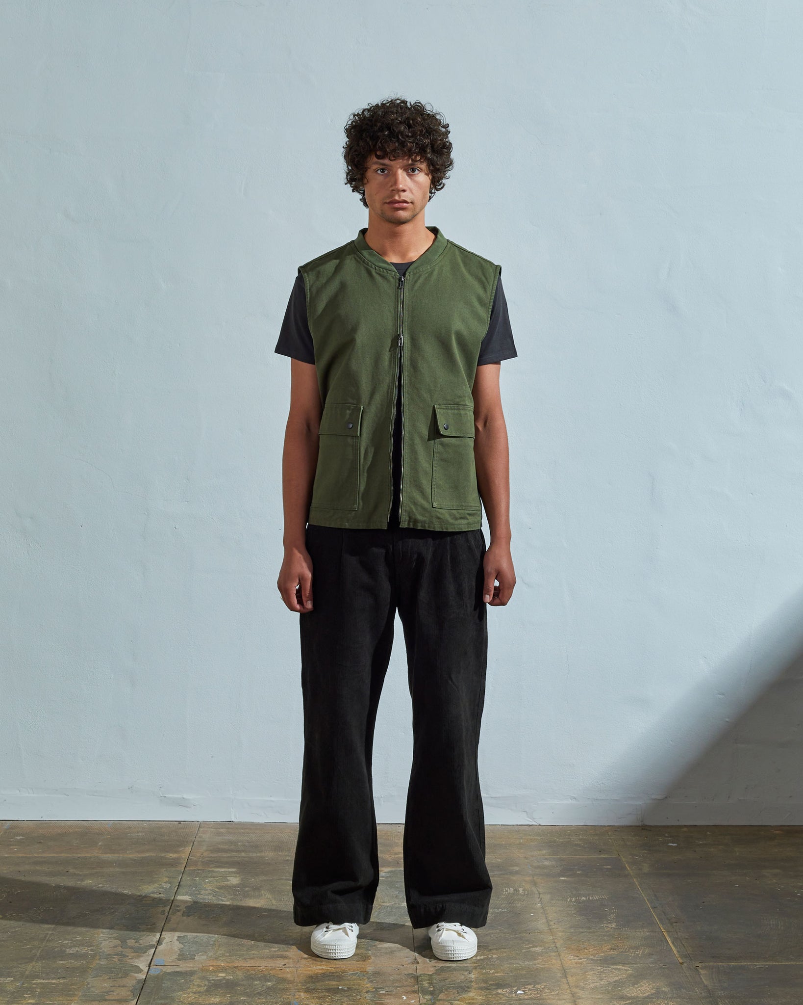 Full-length front view of model wearing #3028 coriander-coloured organic canvas vest paired with dark pants. Half zipped to demonstrate double-ended YKK zip.