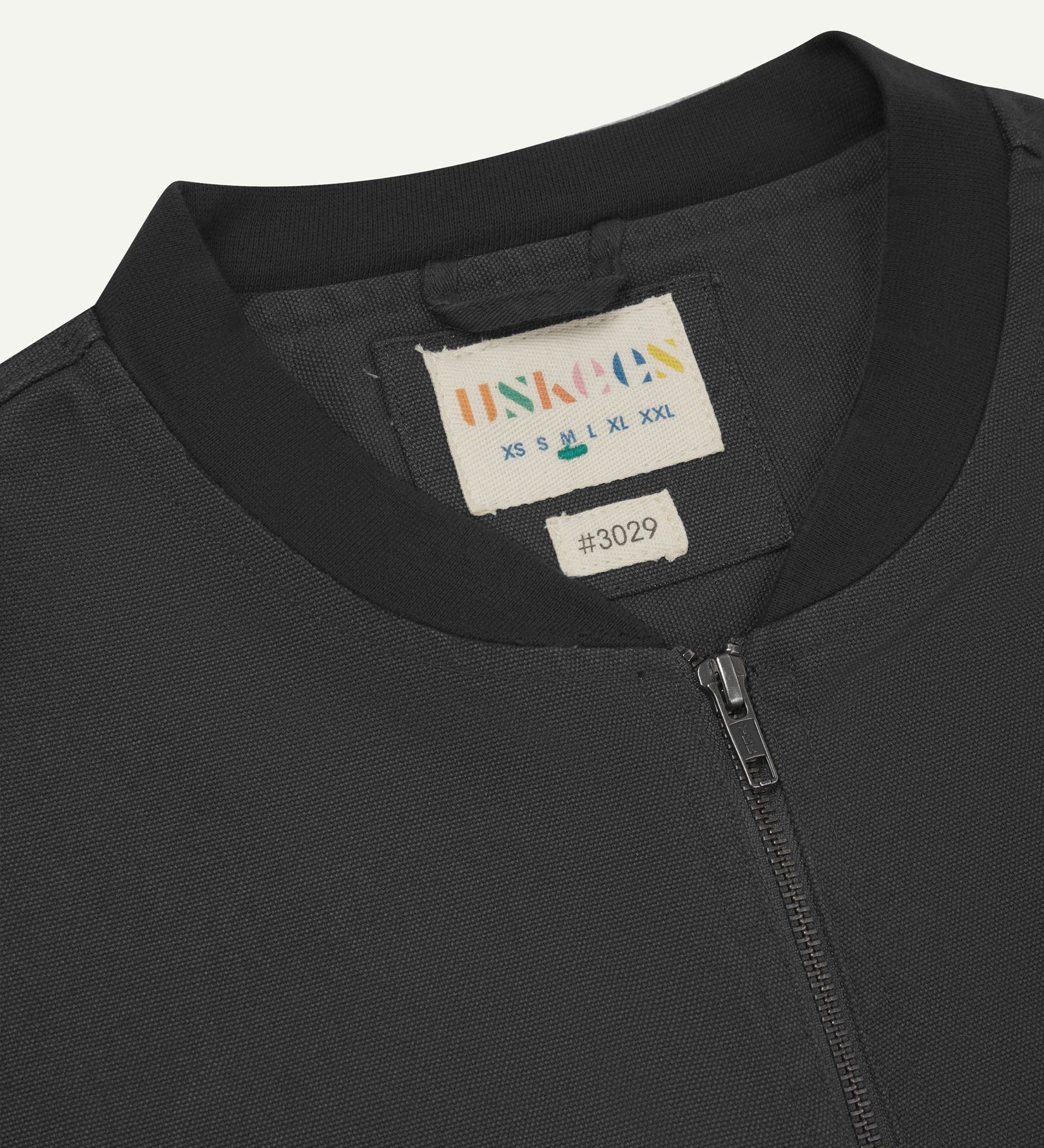 Close-up flat shot of Uskees charcoal-grey gilet-type zip front waistcoat showing jersey cotton collar neck, zip and branding label.