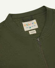 Close-up flat shot of Uskees coriander green gilet-type zip front waistcoat showing jersey cotton collar neck, zip and branding label.