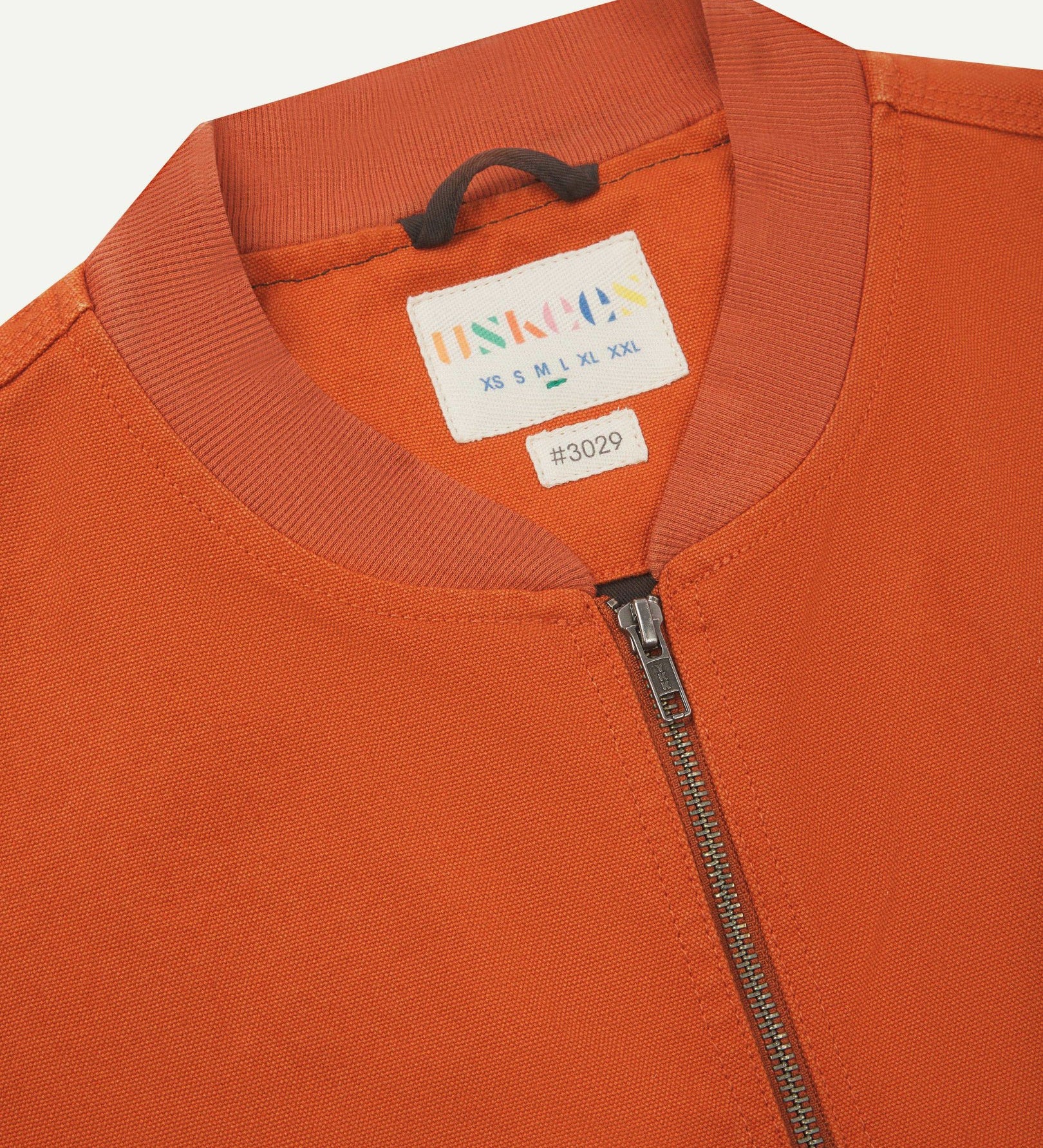 Close-up flat shot of Uskees golden-orange gilet-type zip front waistcoat showing jersey cotton collar neck, zip and branding label.