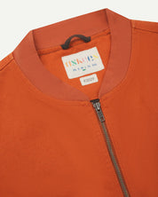 Close-up flat shot of Uskees golden-orange gilet-type zip front waistcoat showing jersey cotton collar neck, zip and branding label.