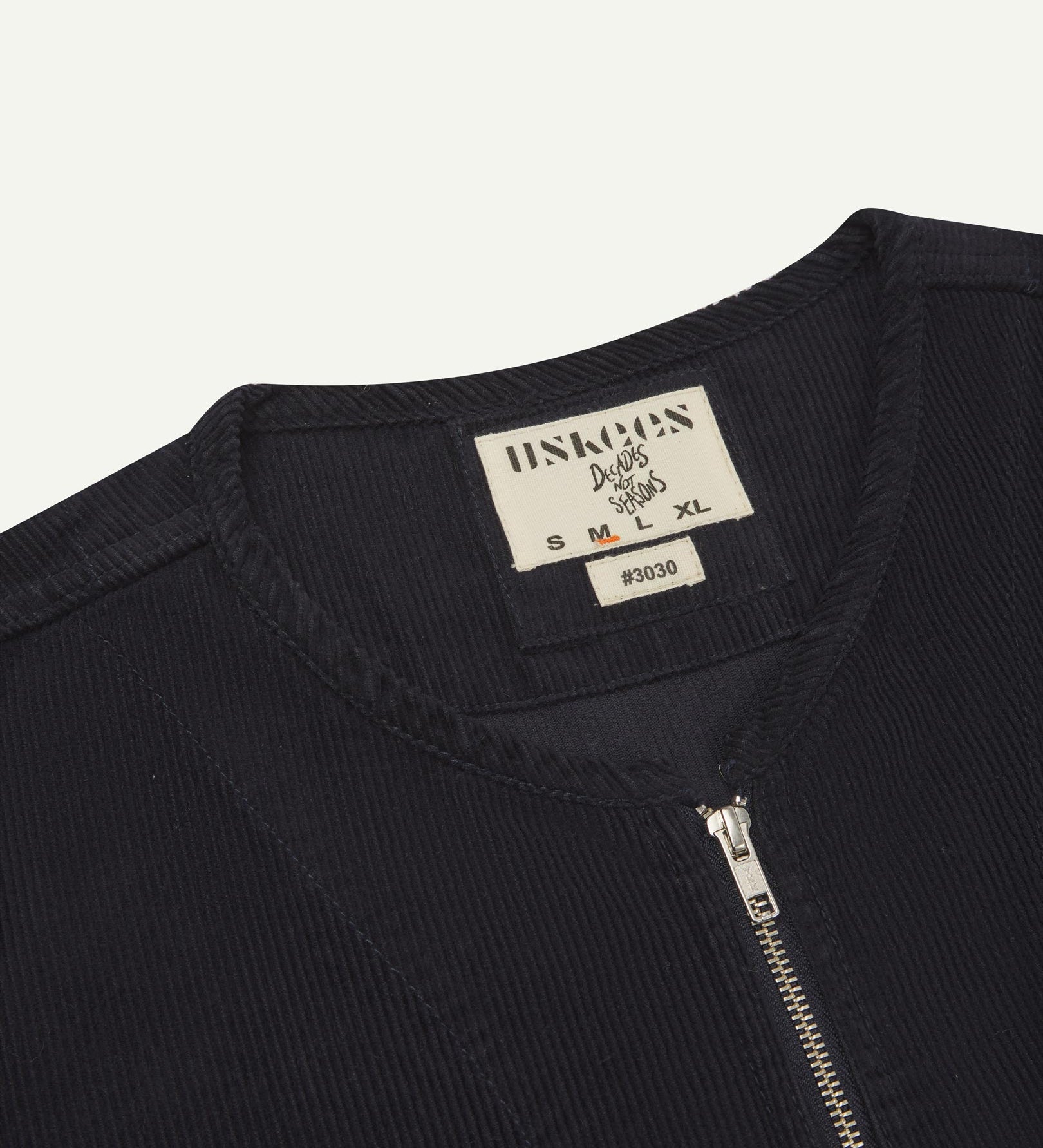 Angled close-up flat view of the neckline detailing of #3030 Uskees midnight blue jacket. View of monochrome Uskees label, 11-wale organic corduroy and YKK zip.