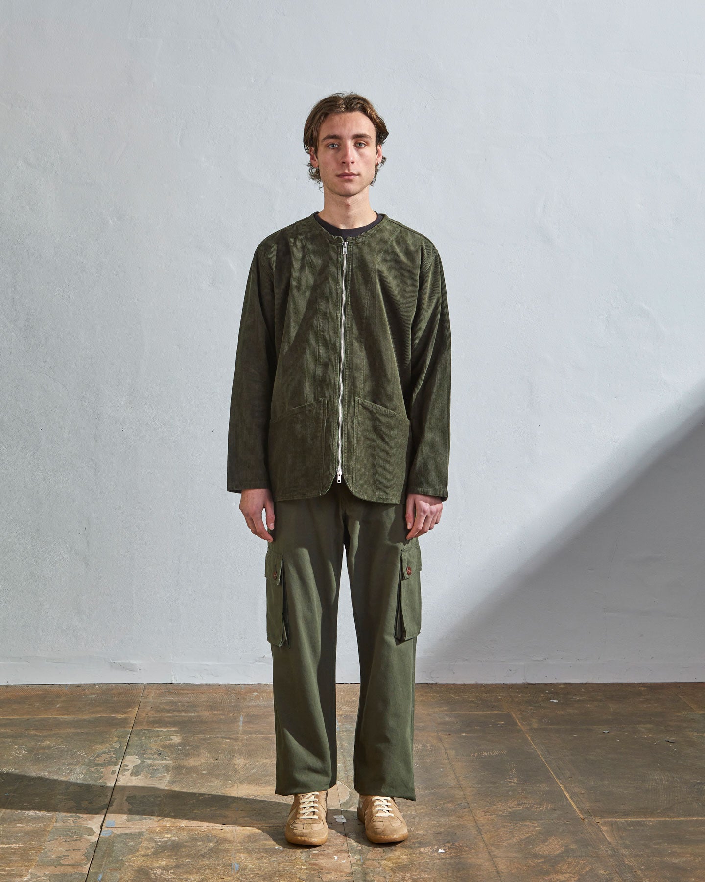 Full-length front view model wearing #5030 Uskees 'vine green' collarless corduroy jacket. Zip fully secured and paired with khaki cargo pants.