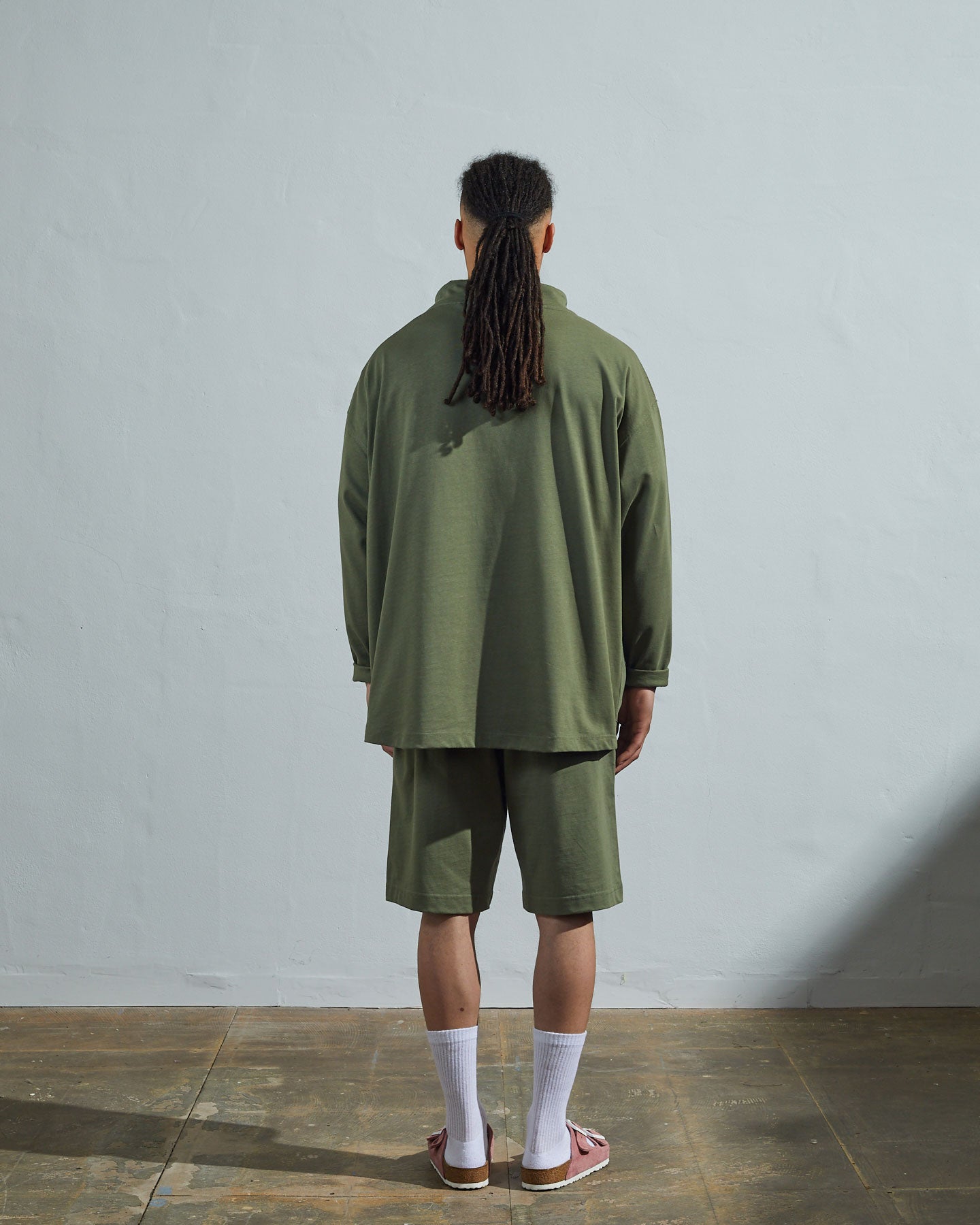 Full-length back view of model wearing army green, relaxed cut organic cotton #3032 jersey tie neck smock by Uskees showing simple loose boxy design.