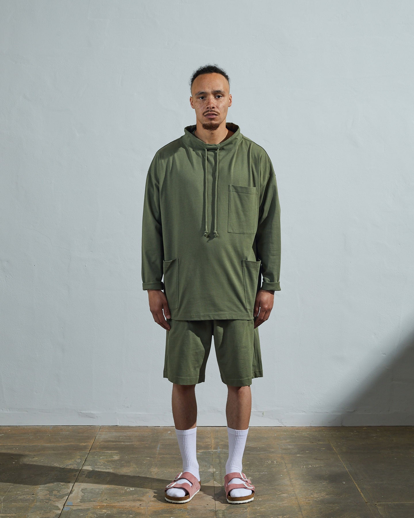 Full-length front view of model wearing army green organic cotton #3032 jersey tie neck smock by Uskees with clear view of funnel neck styling.