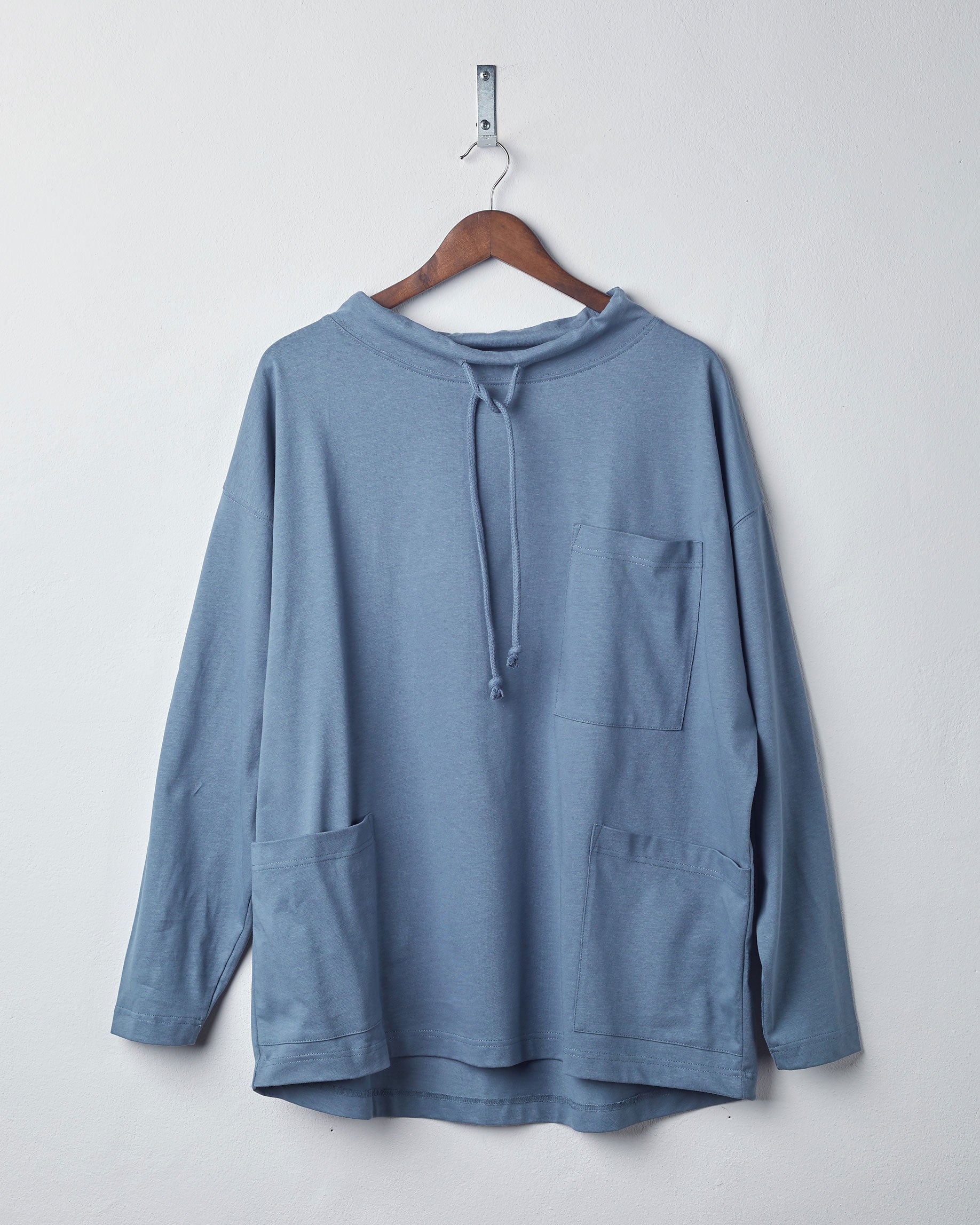 Front view of teal organic cotton #3032 jersey tie neck smock by Uskees, presented on hanger against white background. 