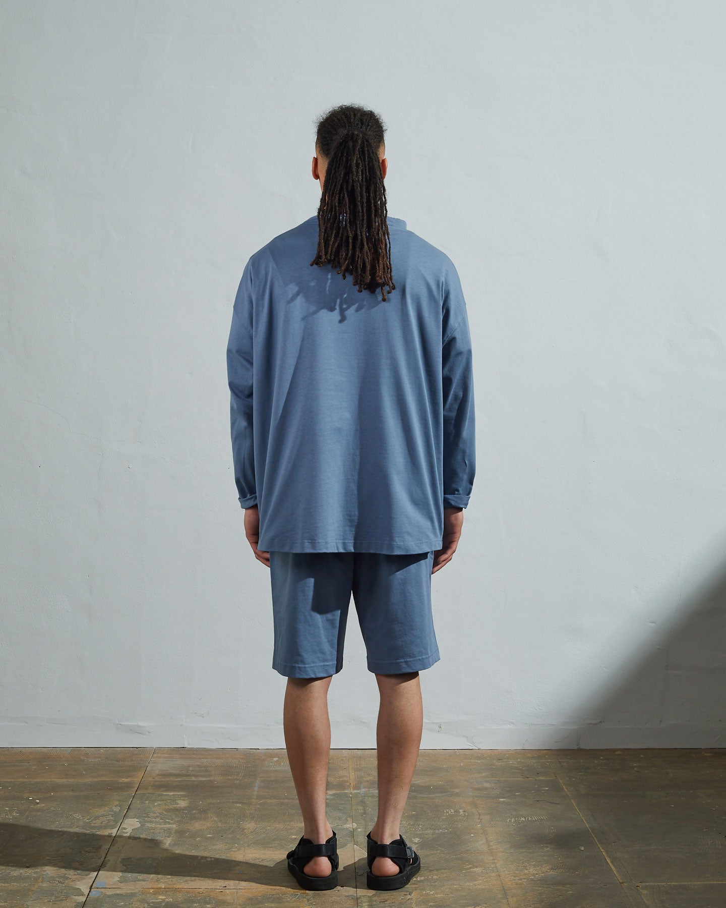 Full-length back view of model wearing teal, relaxed cut organic cotton #3032 jersey tie neck smock by Uskees showing simple loose boxy design.