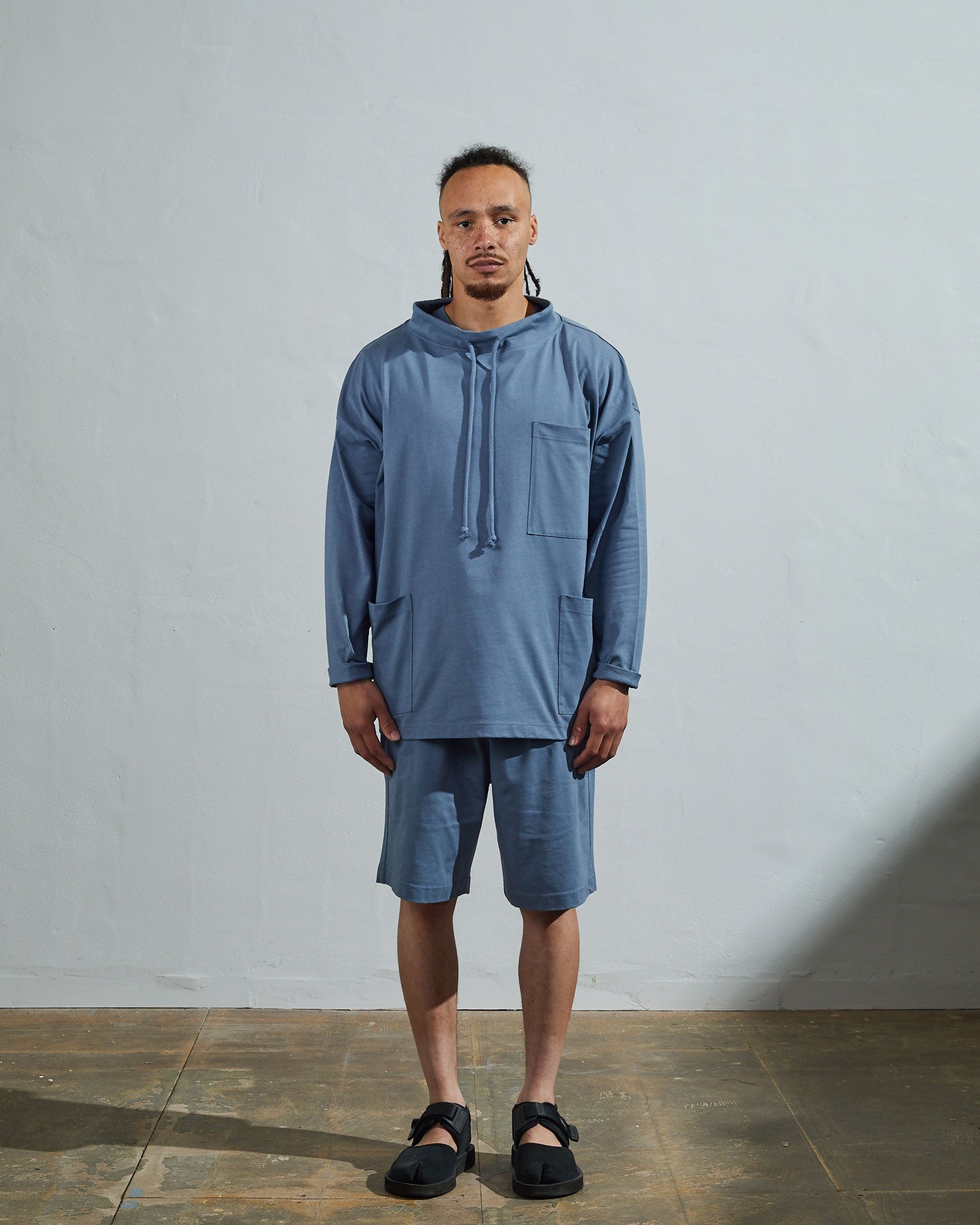 Full-length front view of model wearing teal organic cotton #3032 jersey tie neck smock by Uskees with clear view of funnel neck styling.