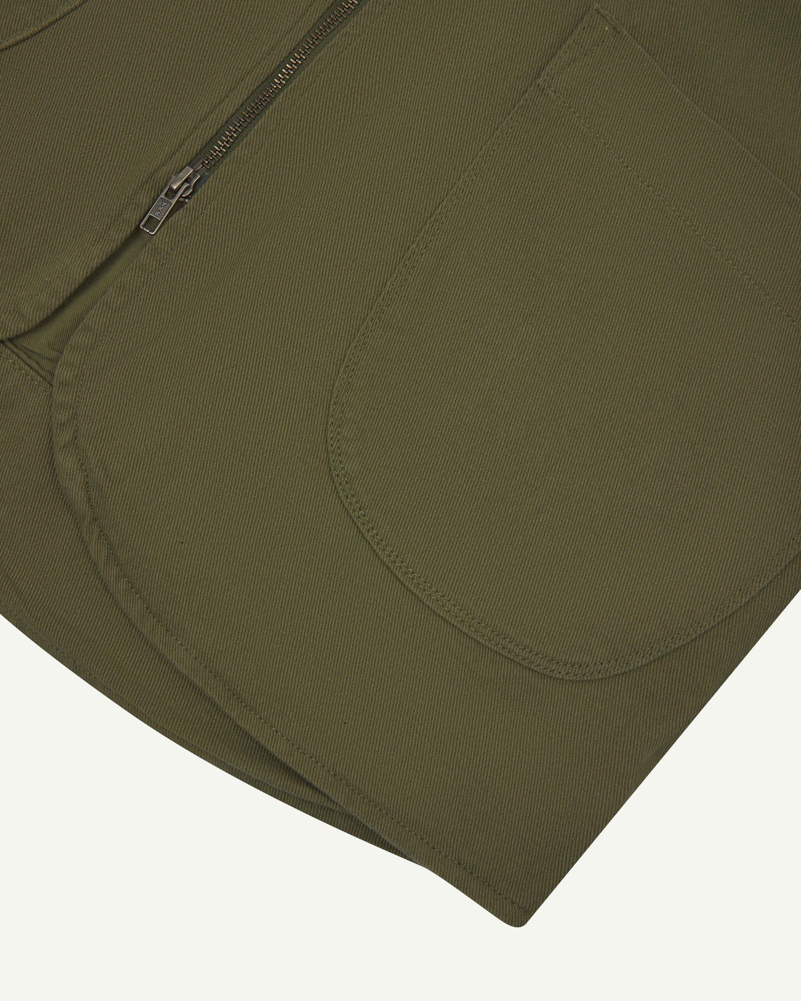 Close-up bottom-half view of #3036 moss-green organic cotton-drill vest with focus on curved pocket detail.