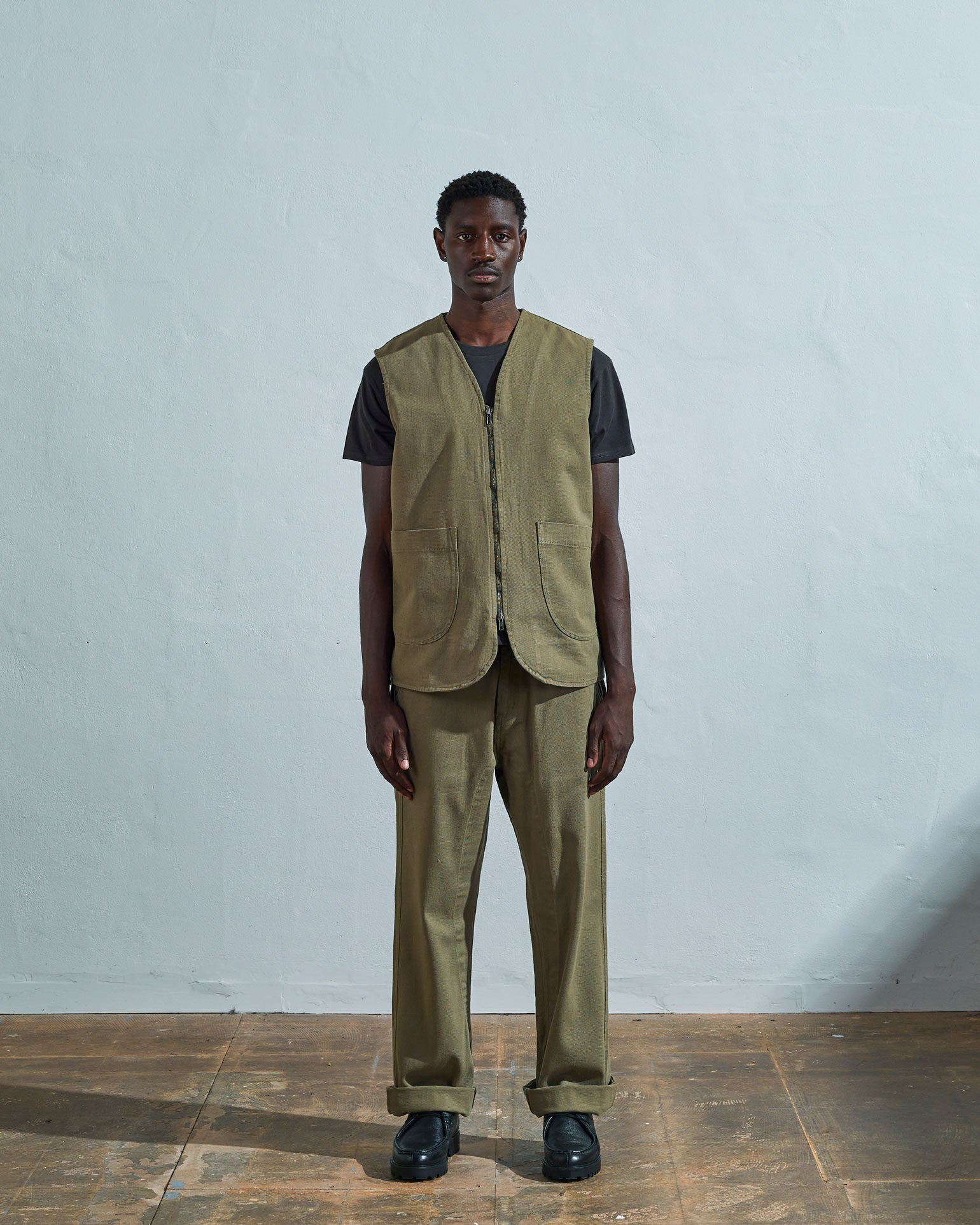 Full-length front view of model wearing fully zipped #3036 moss-green organic cotton-drill vest paired with matching Uskees pants.