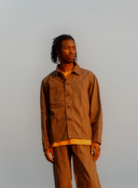 Front view of model wearing Uskees dark taupe  organic herringbone cotton engineer jacket with matching Uskees pants.