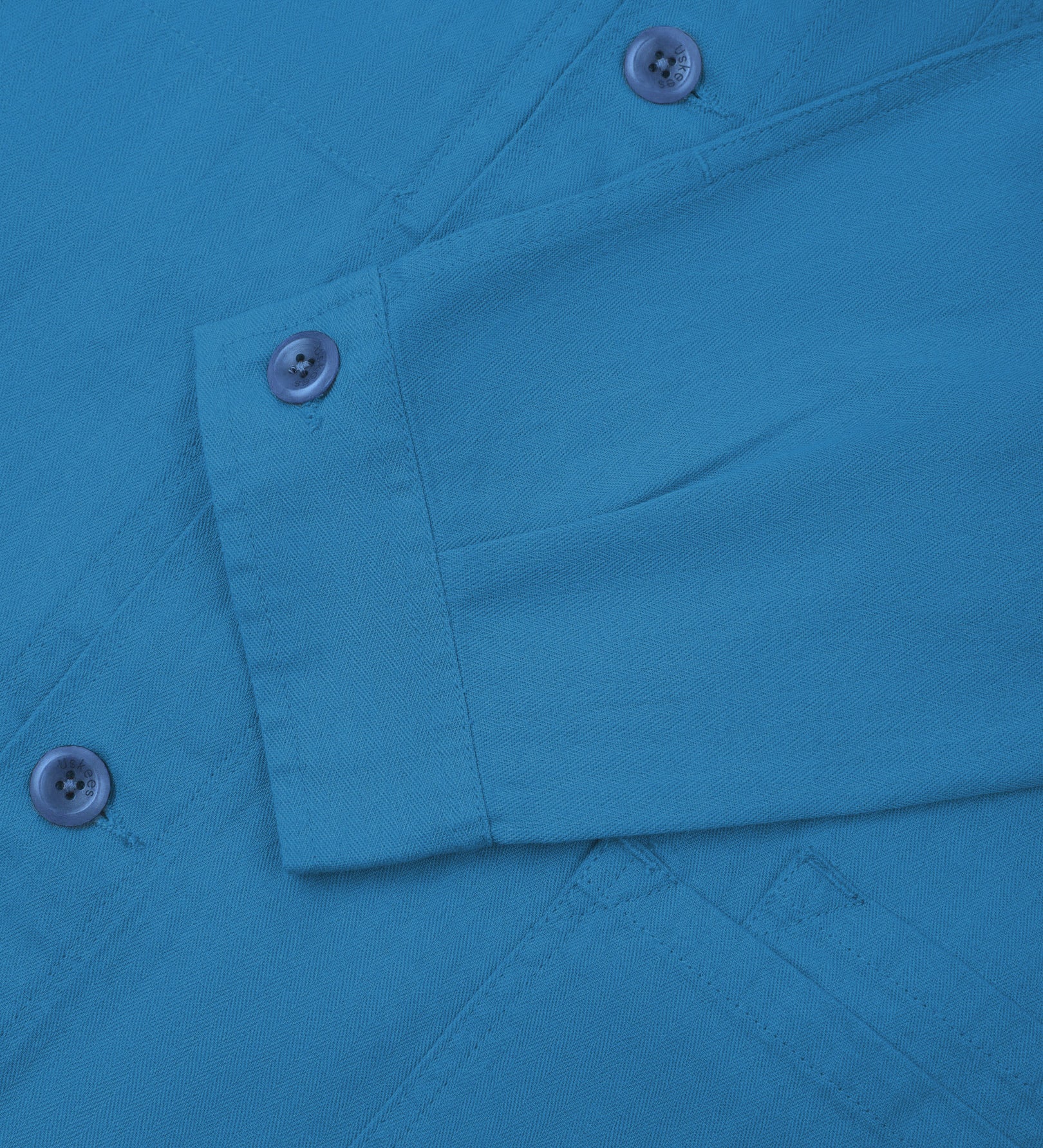 Sleeve view of Uskees 3040 opal-blue herringbone cotton engineer jacket with focus on placket, buttoned cuff and ticket pocket.