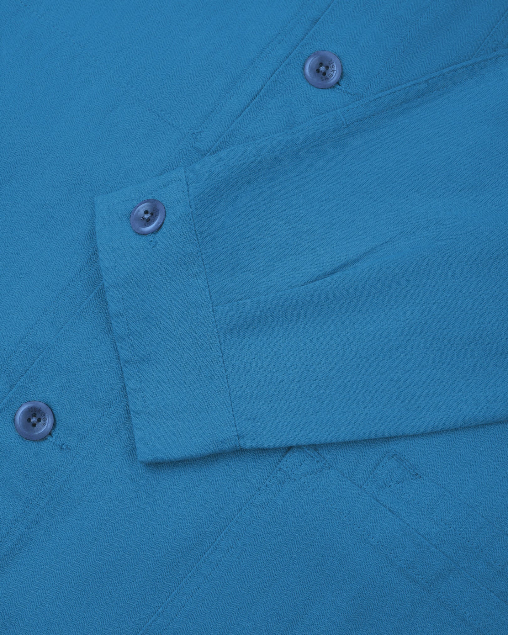 Sleeve view of Uskees 3040 opal-blue herringbone cotton engineer jacket with focus on placket, buttoned cuff and ticket pocket.