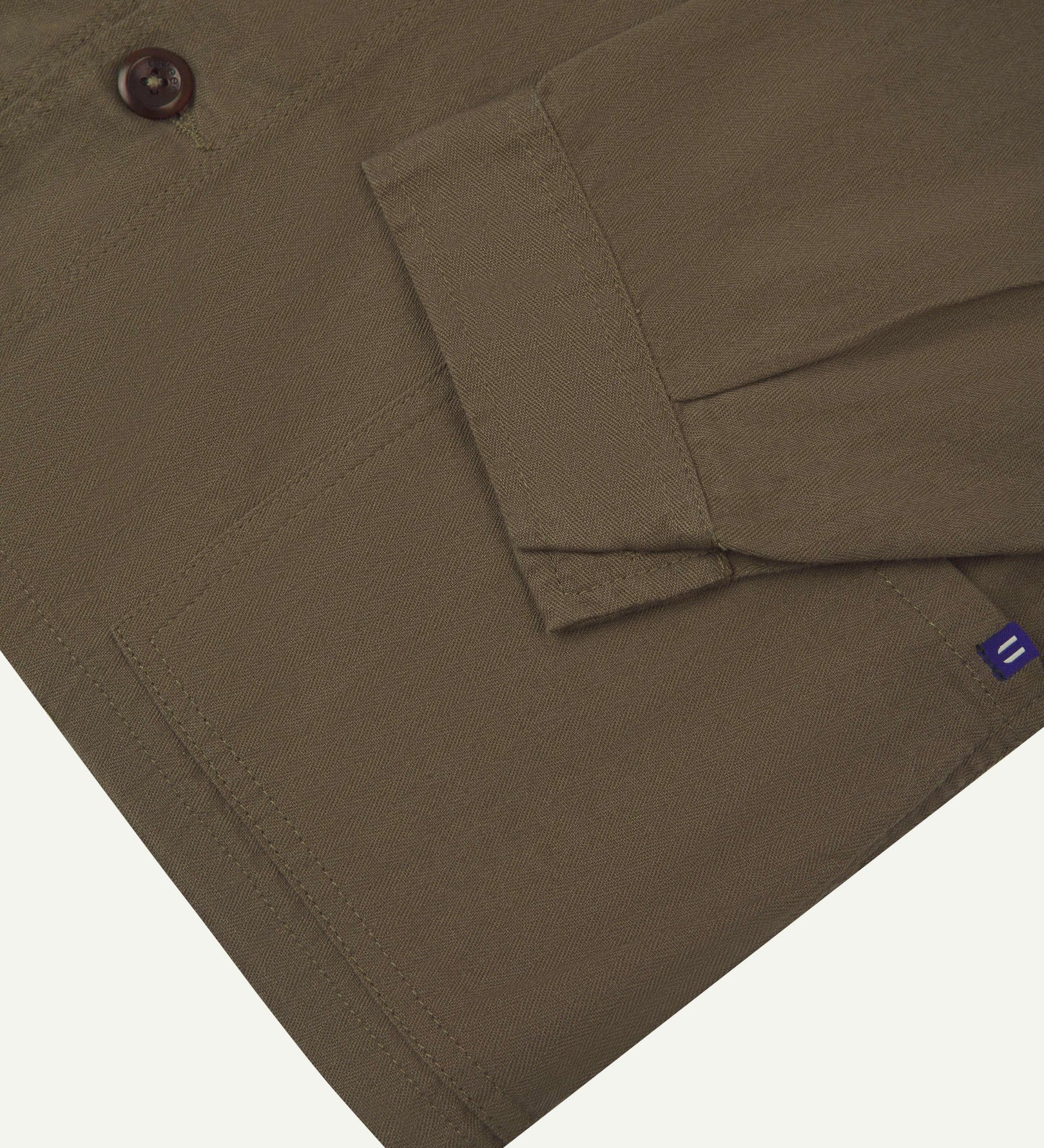 Close-up view of one of two hip pockets, cuff and Uskees branding tag of the 3041 signal jacket. Also is a closer view of the herringbone texture of the dark taupe cotton. 