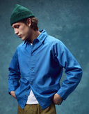Top-half view of model wearing organic cotton opal-blue signal jacket from Uskees. Paired with Uskees beanie and khaki-green pants.