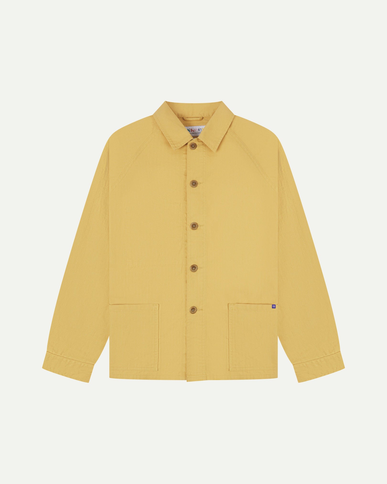 Flat front view of organic cotton sandstone-yellow signal jacket from Uskees. Clearly showing the corozo button fastening and 2 deep hip pockets.