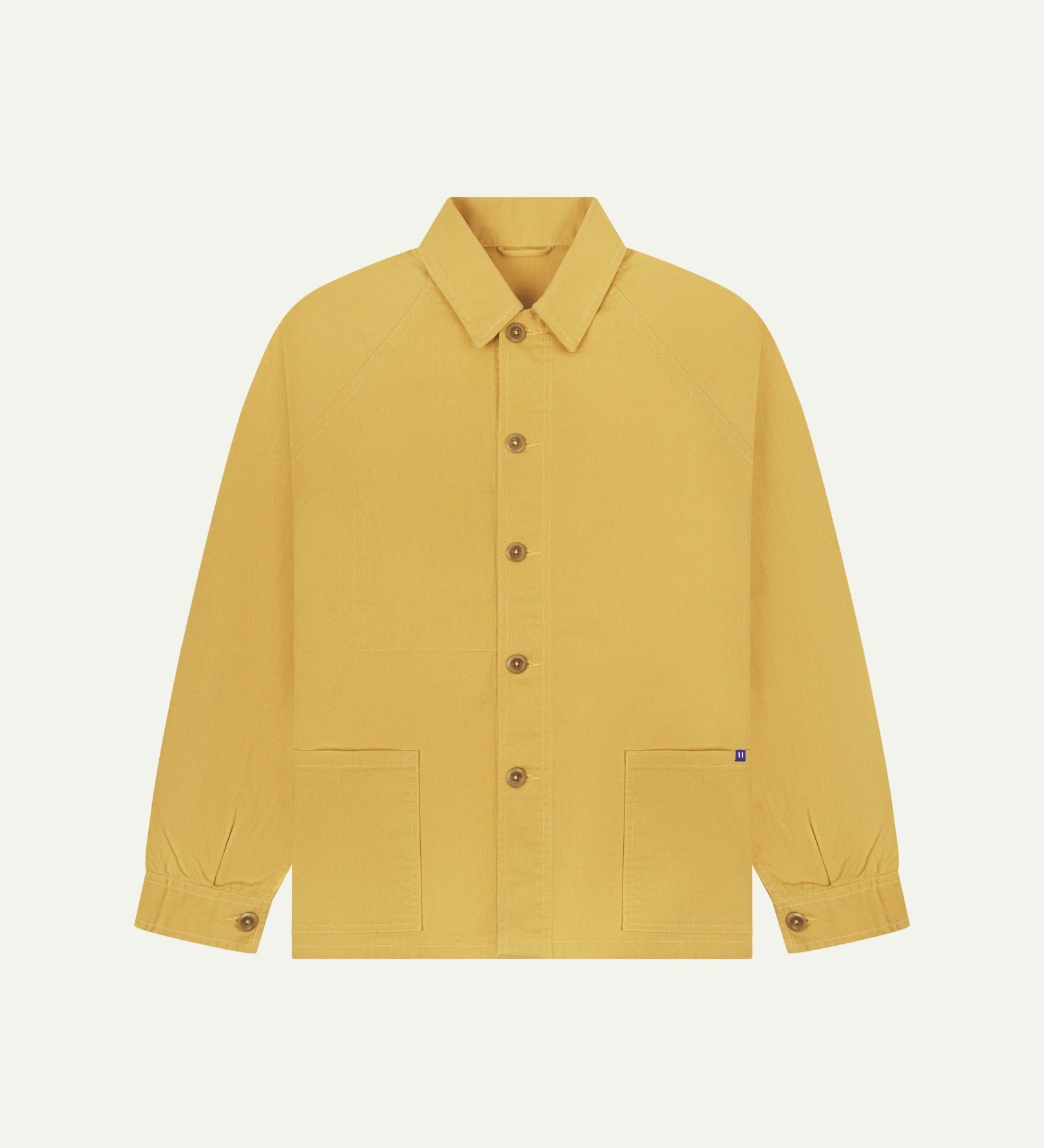 Flat front view of organic cotton sandstone-yellow signal jacket from Uskees. Clearly showing the corozo button fastening and 2 deep hip pockets.