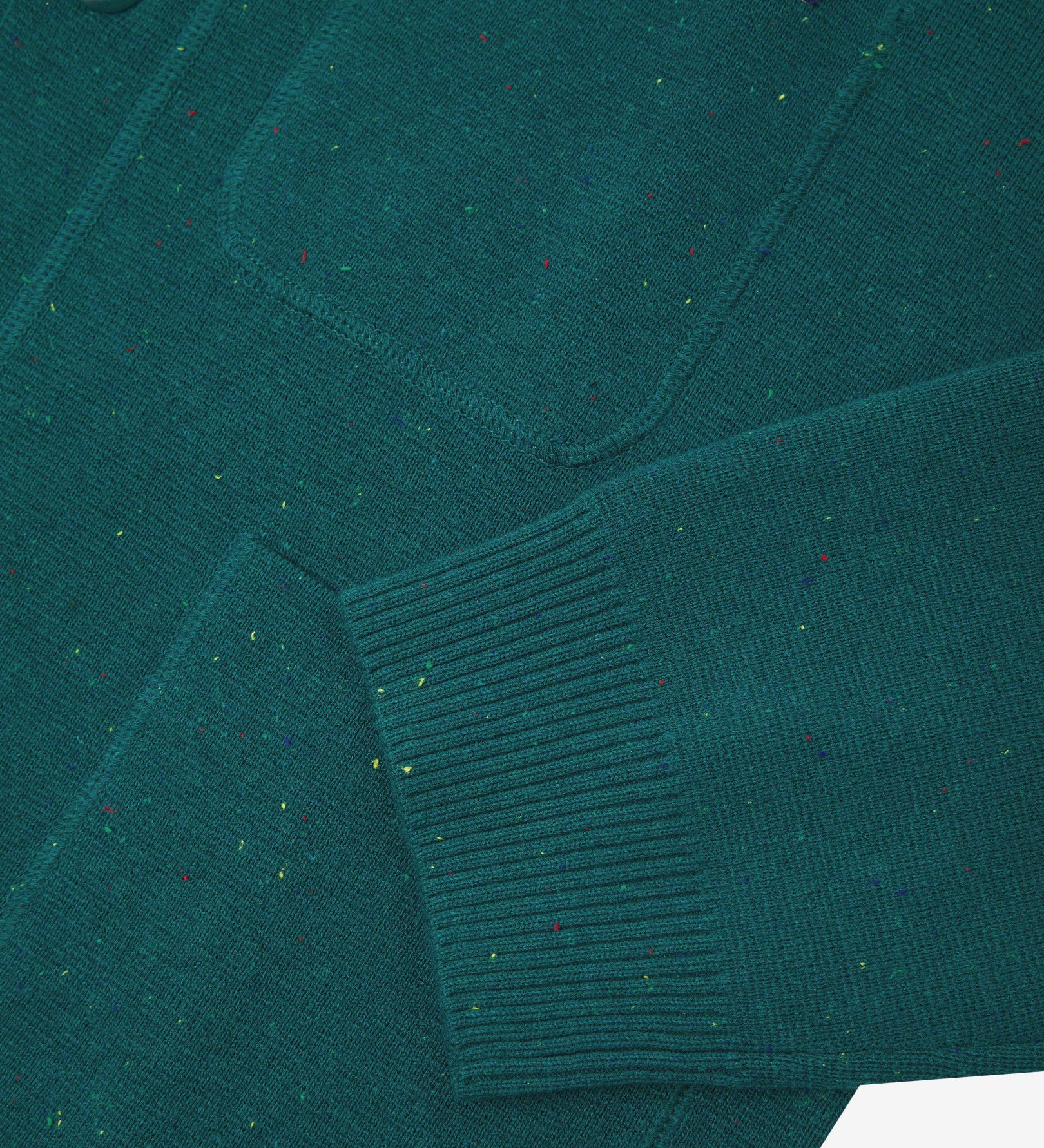 Close-up view of ribbed cuff and pockets of the knitted organic cotton, foam green cardigan. Discreet Uskees branding label visible on chest pocket.