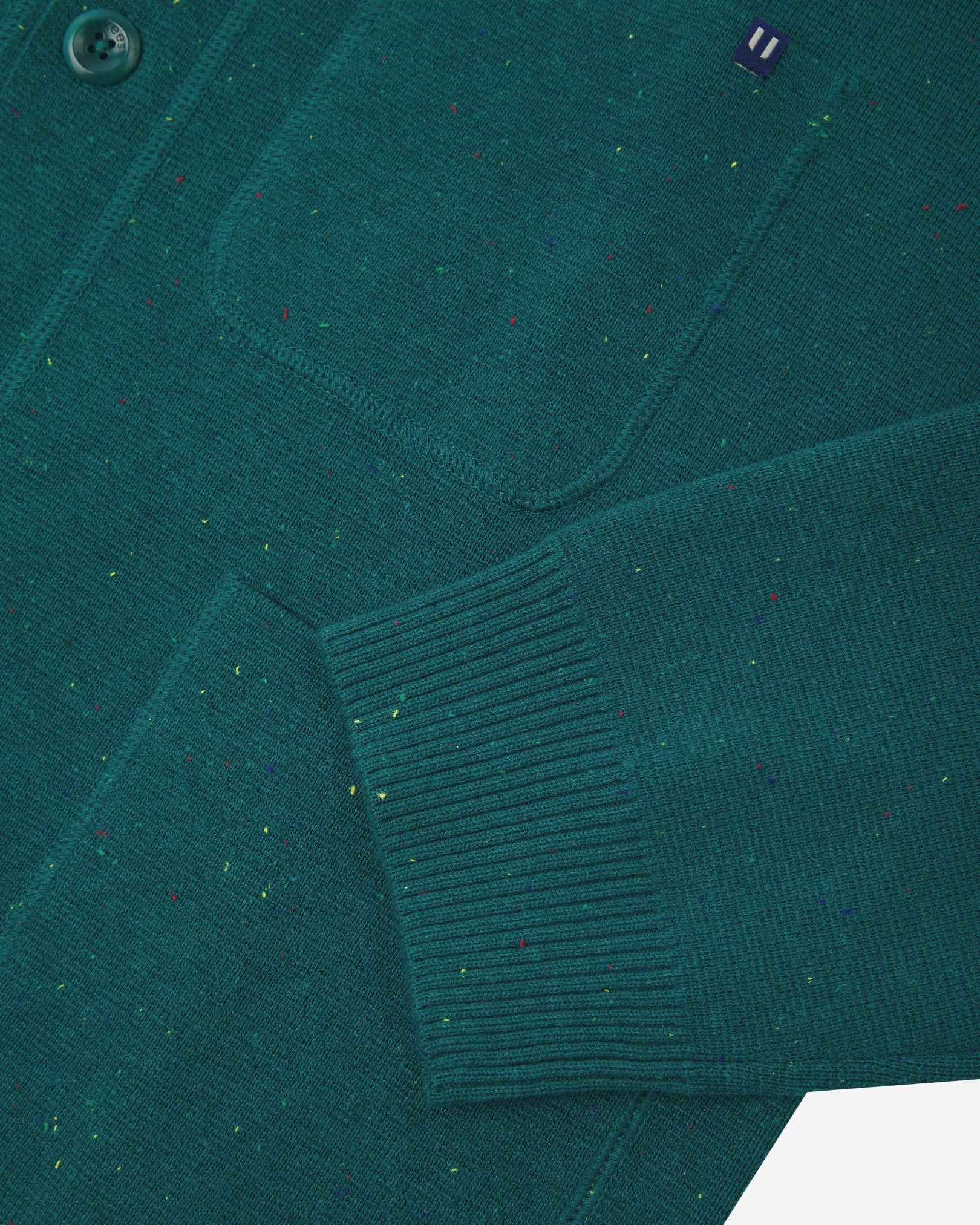 Close-up view of ribbed cuff and pockets of the knitted organic cotton, foam green cardigan. Discreet Uskees branding label visible on chest pocket.