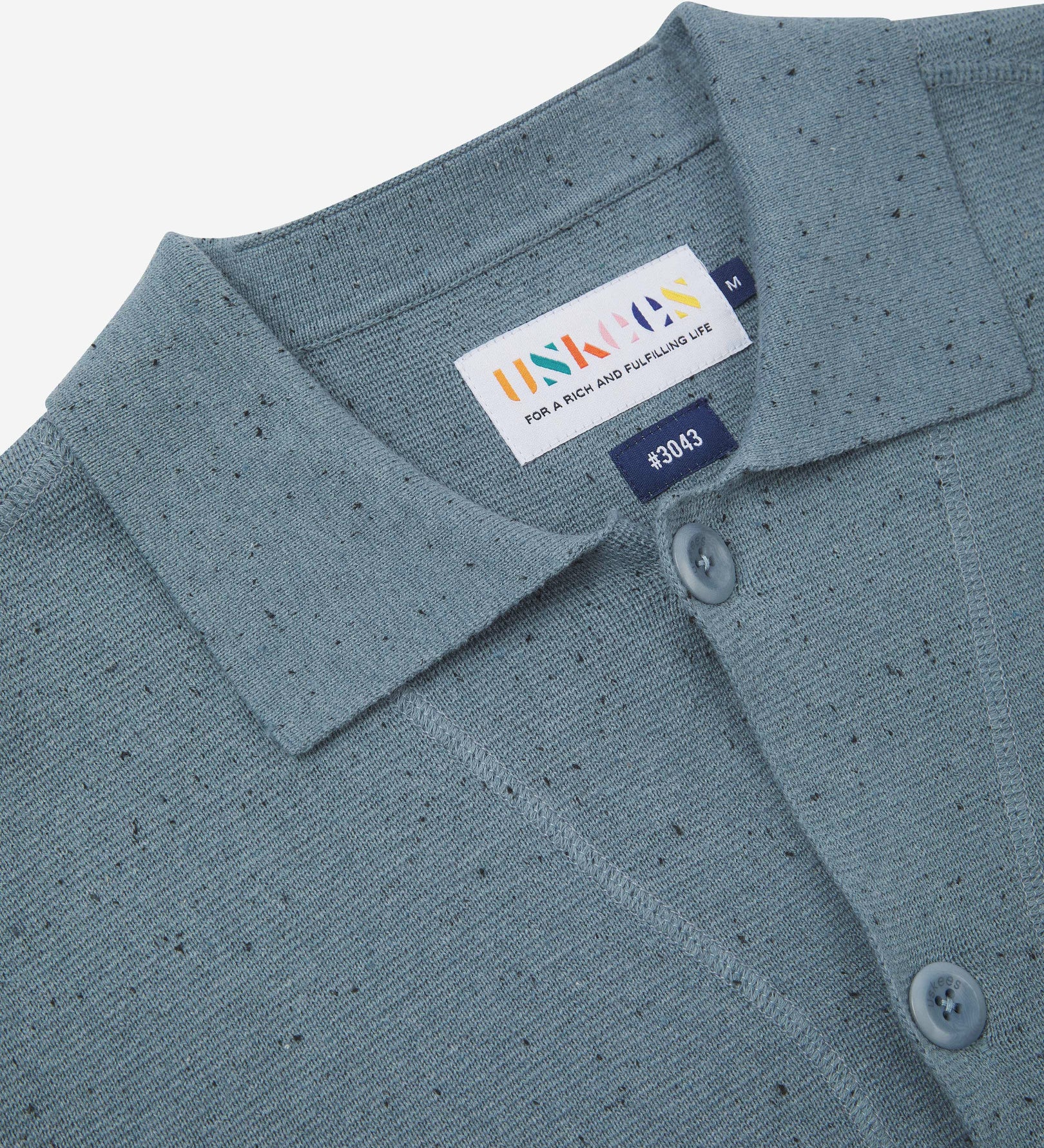 Close-up front view of knitted organic cotton blue-grey cardigan showing the collar, corozo buttons and Uskees branding label.