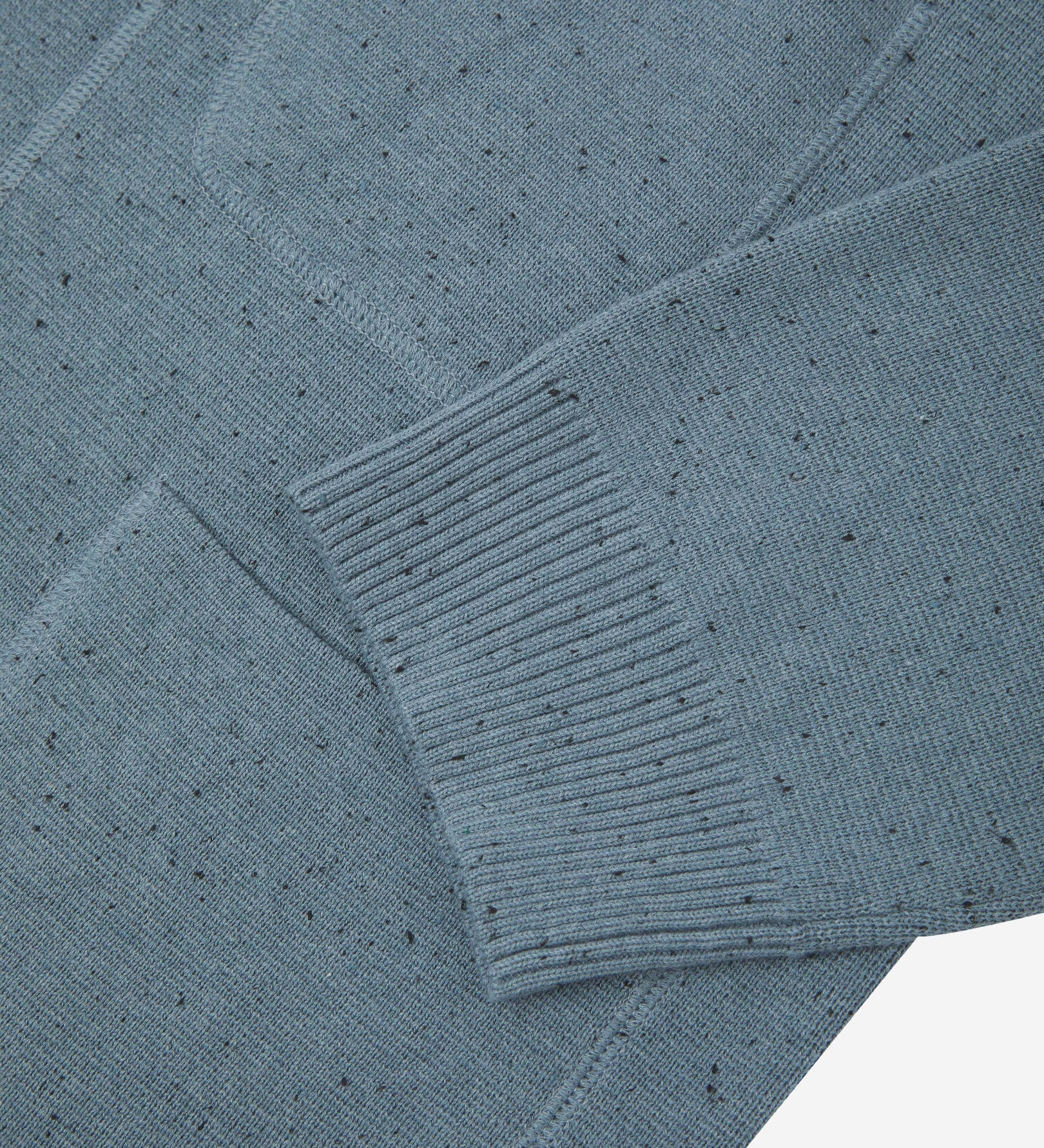 Close-up view of ribbed cuff and pockets of the knitted organic cotton, blue-grey cardigan. Discreet Uskees branding label visible on chest pocket.